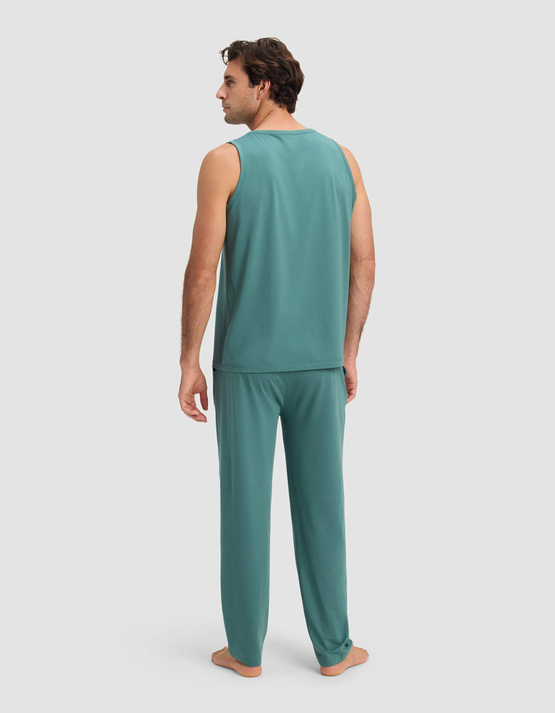 A man stands barefoot, facing away, wearing the Cozy Earth Men's First Layer Pajama Tank & Pant Set in teal against a plain light background.