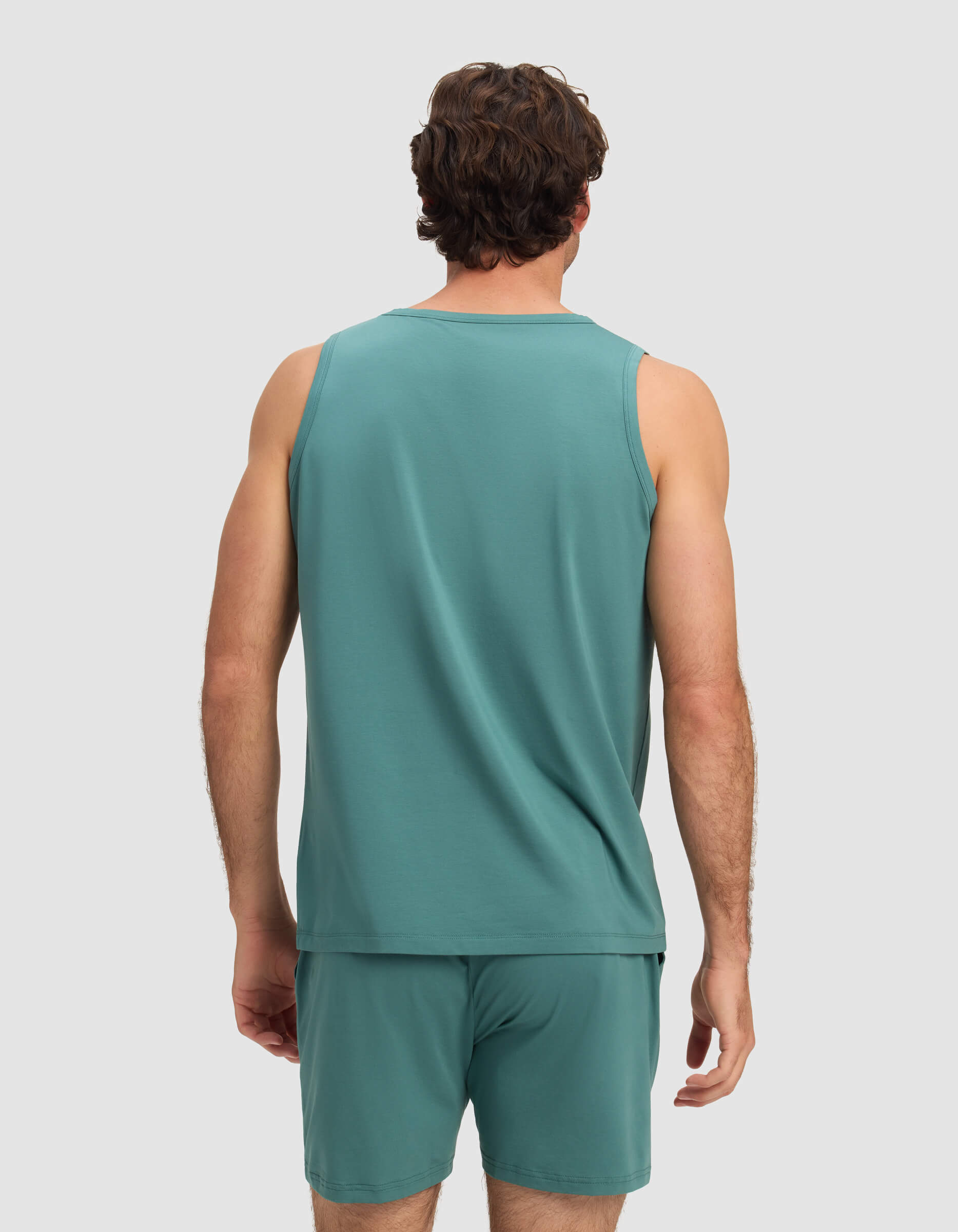 A man with short brown hair, seen from behind, wears the Cozy Earth Men's First Layer Pajama Tank in teal against a plain light gray background.