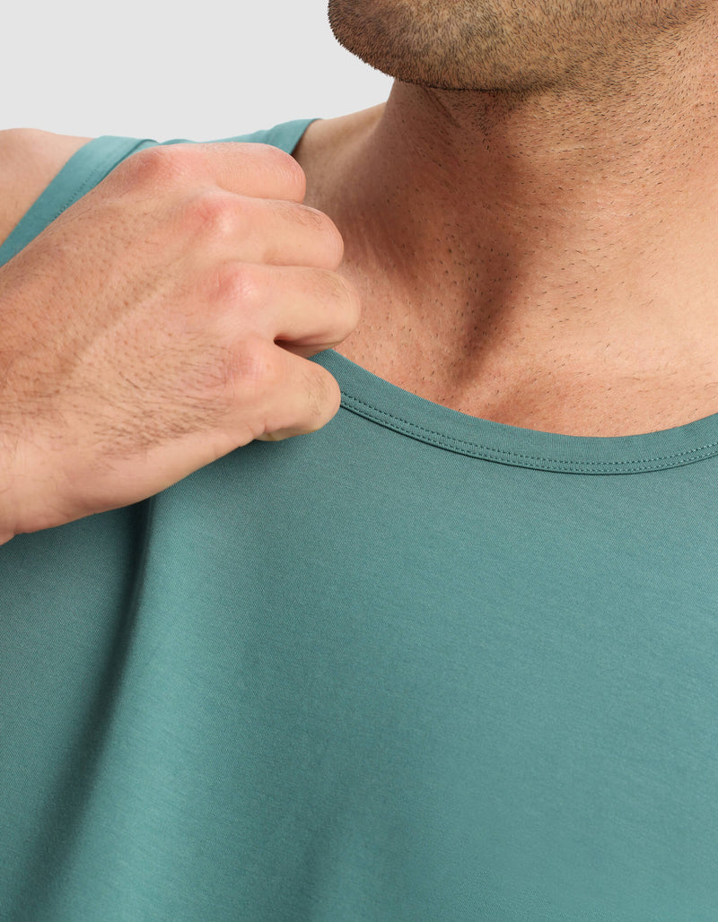 A close-up shows a person wearing the Cozy Earth Men's First Layer Pajama Tank in teal, holding the fabric near their shoulder with their right hand, with only the lower half of their face visible.
