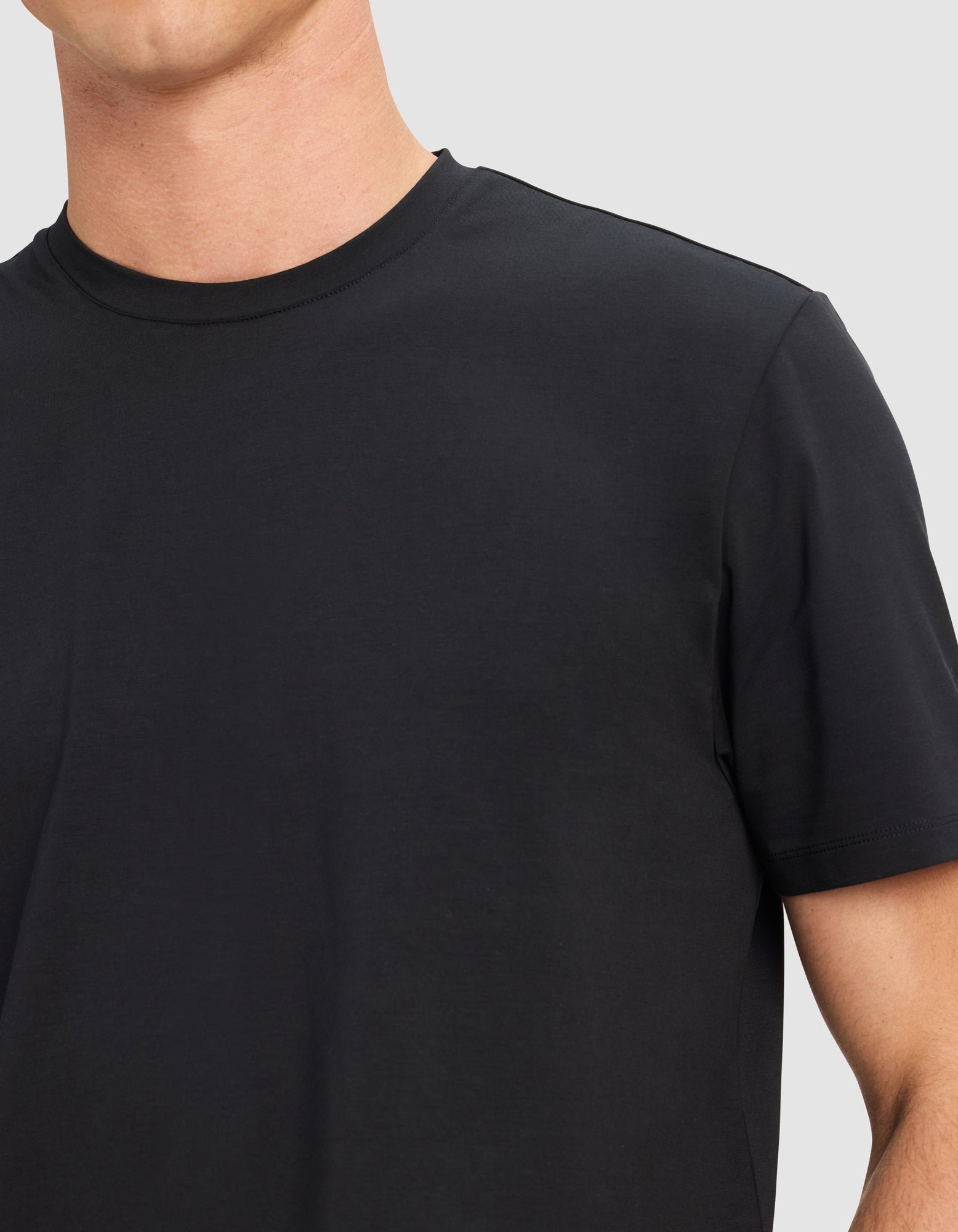 A person wears the Cozy Earth Men's First Layer Pajama Short Sleeve Tee; only the upper torso and part of the left arm are visible against a light gray background.|Color:Jet Black