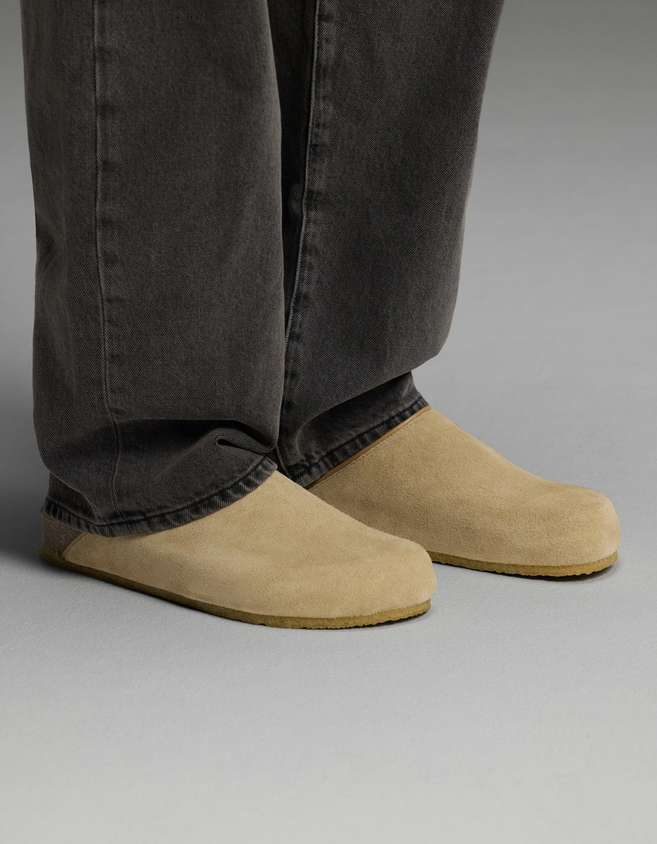 A person wearing loose, dark-colored pants and Cozy Earth’s Lakehouse Clog in Suede stands on a light gray surface.