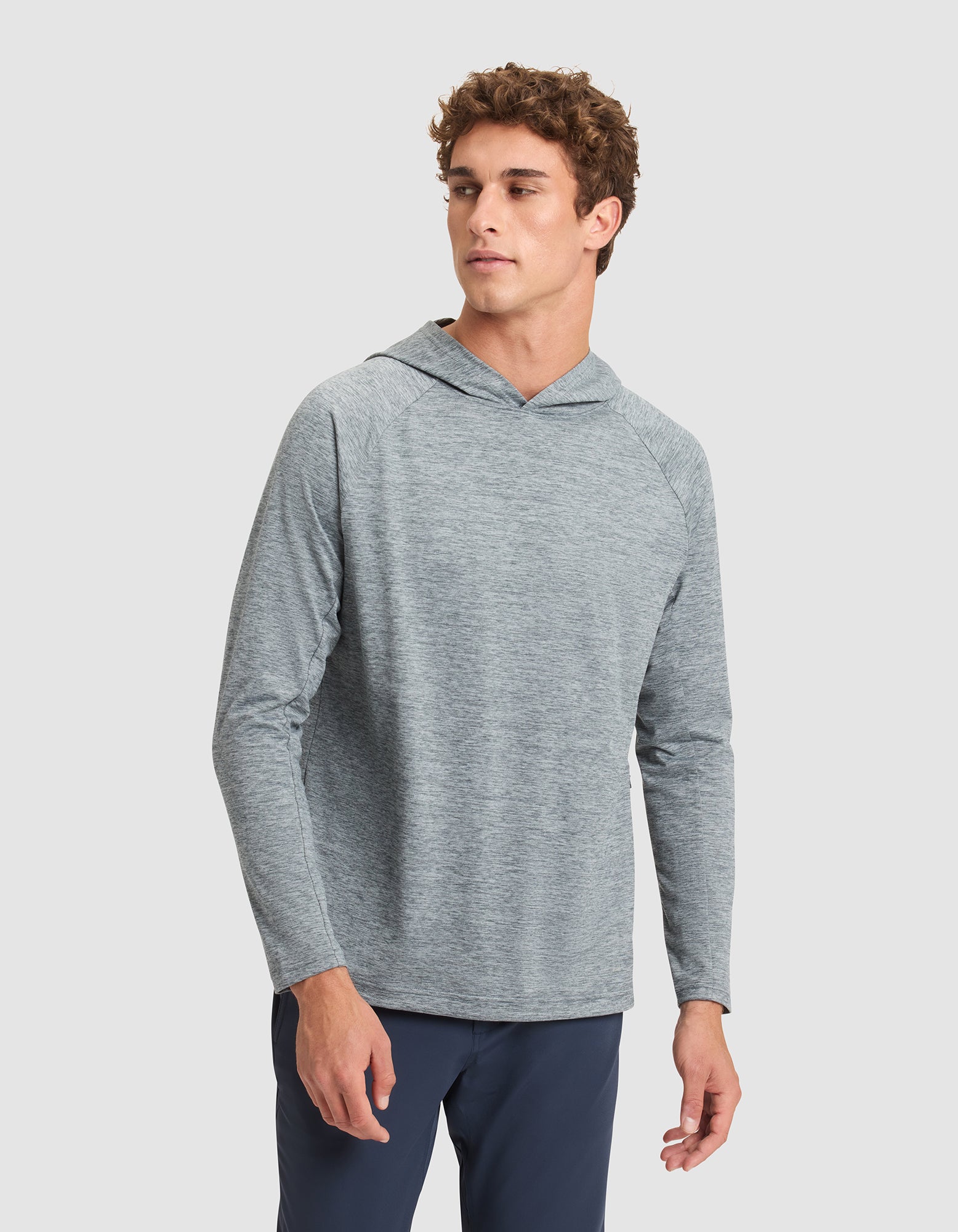 A man models the Cozy Earth Men's Lightweight Performance Hoodie in light gray with dark pants, standing against a plain light background and looking slightly left with a neutral expression. 