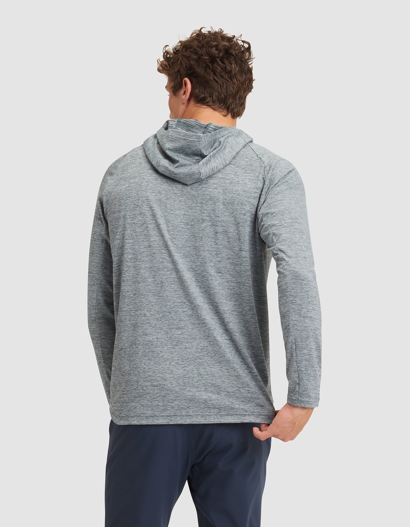 A man with curly hair, seen from behind against a white background, wears the Cozy Earth Men's Lightweight Performance Hoodie in light gray and navy pants. 
