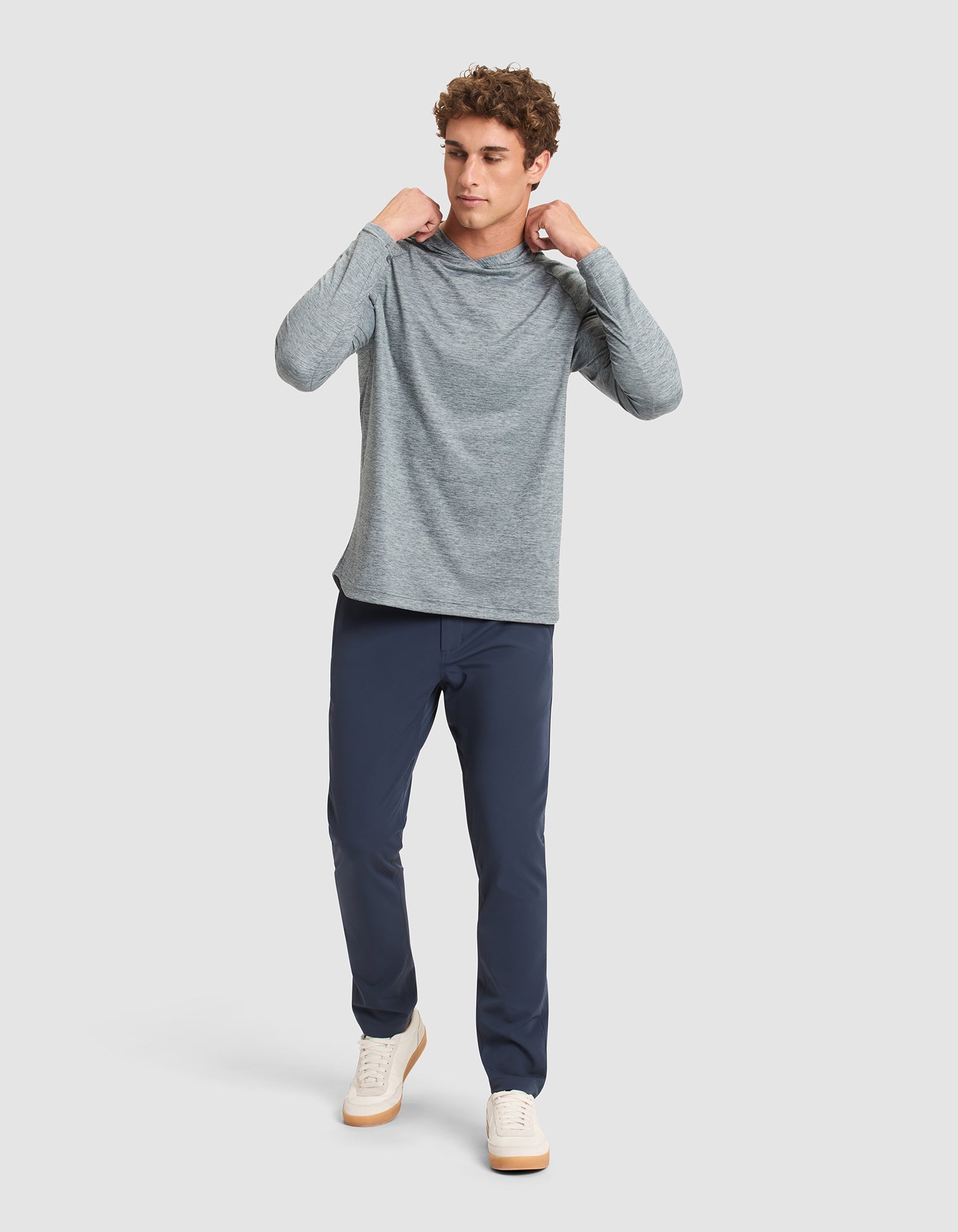A man stands against a plain background, wearing the Cozy Earth Men's Lightweight Performance Hoodie. He looks to the side, holding the hoodie’s collar with both hands. 