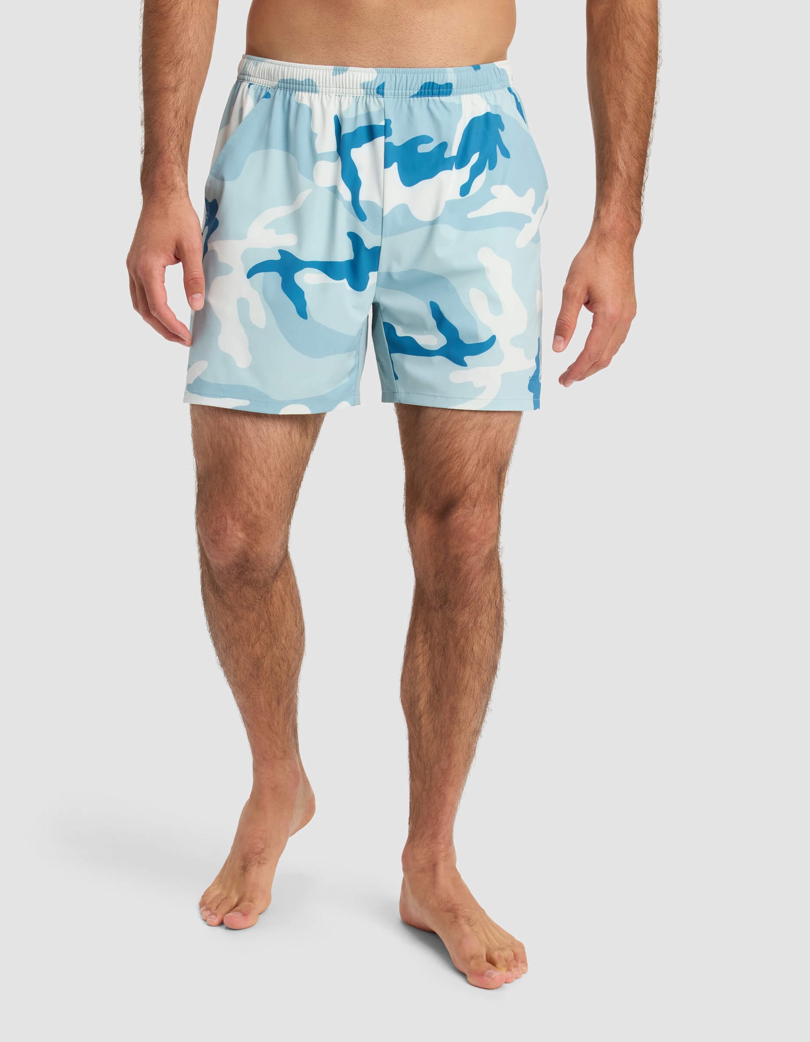 A barefoot man models Cozy Earth’s Men’s Day & Night Short 5" in a light blue, white, and dark blue camo print with an elastic waistband. His upper body is out of frame against a plain white background.