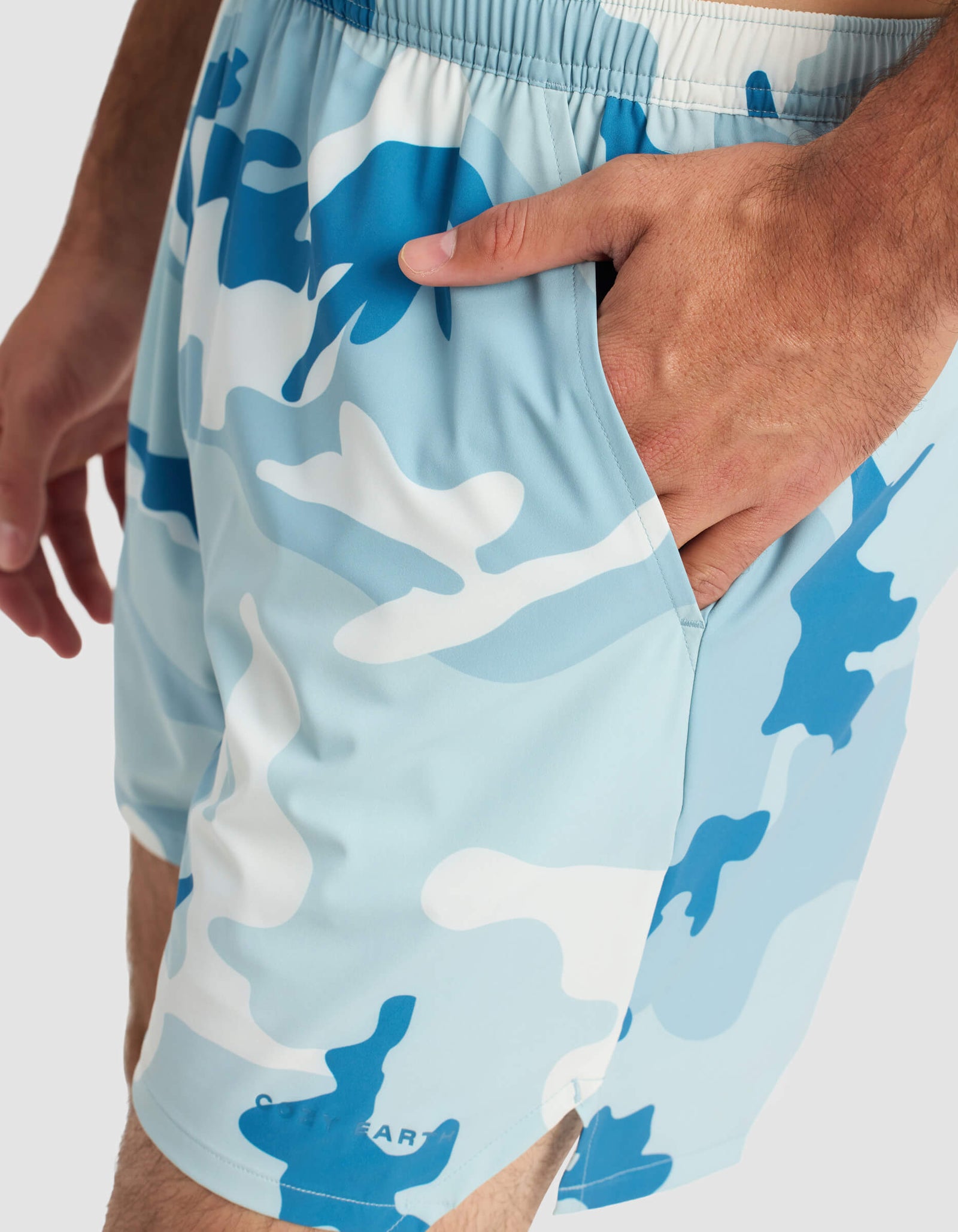 A close-up of a person wearing Cozy Earth Men's Day & Night Short 5" in blue and white camo with one hand in the pocket, featuring an elastic waistband and "COASTAL" near the hem.
