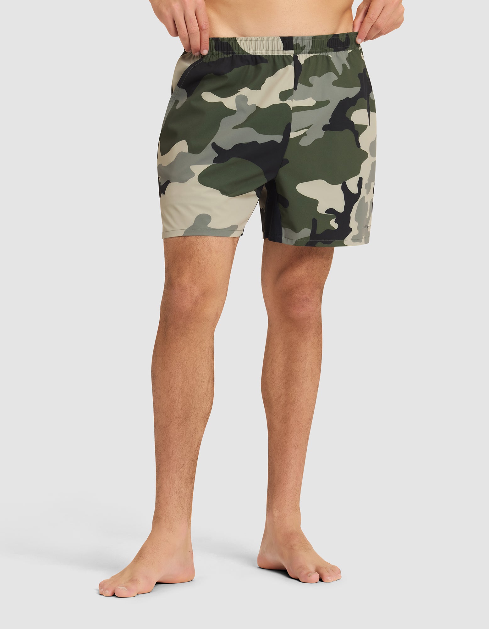 A person stands barefoot in Cozy Earth Men's Day & Night Shorts 5" against a plain light background, showing only the lower torso and legs. 