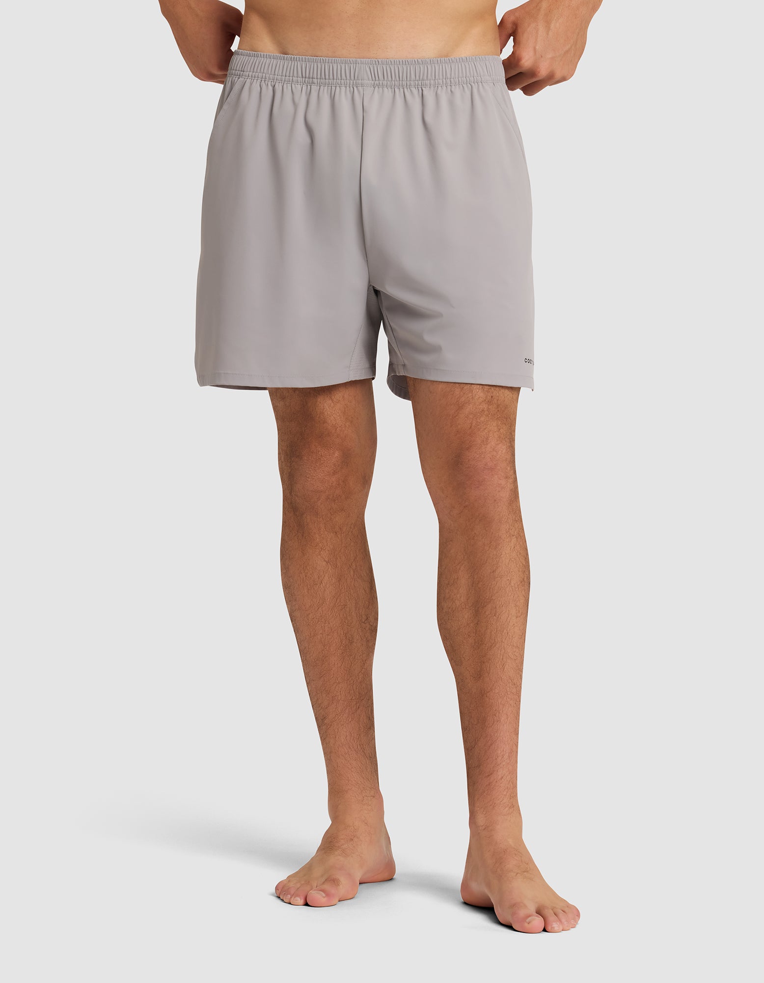 A person stands barefoot wearing the Cozy Earth Men's Performance Sleep Short in light gray, featuring an elastic waistband. The image is cropped from the waist down against a plain white background. |Color:Stone