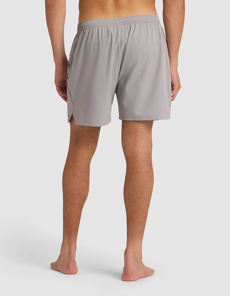 A man stands barefoot, facing away from the camera, wearing Cozy Earth Men's Performance Sleep Shorts in light gray with an elastic waistband, set against a plain white background.