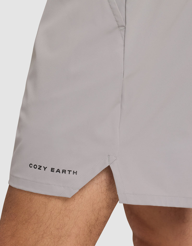 A close-up of a person wearing Cozy Earth Men's Performance Sleep Shorts in light gray, featuring the brand name near the left hem, a small side slit, and a visible pocket seam.