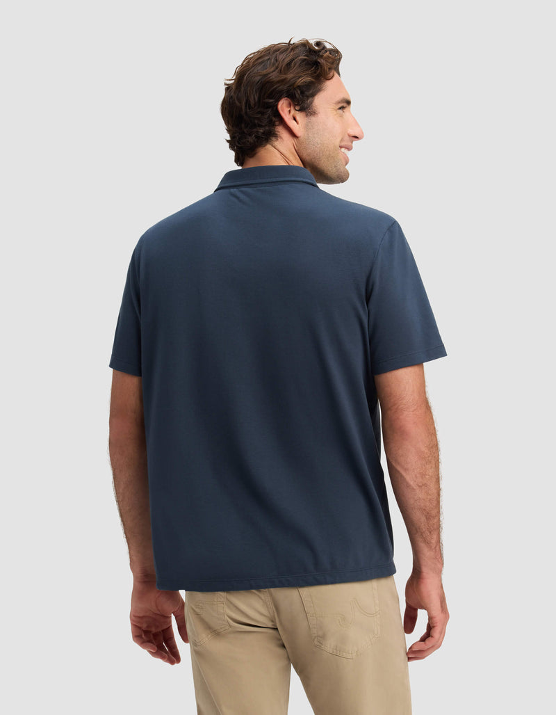 A man faces away, wearing Cozy Earth's Men's Pique Polo in navy with beige pants, set against a plain light gray background.