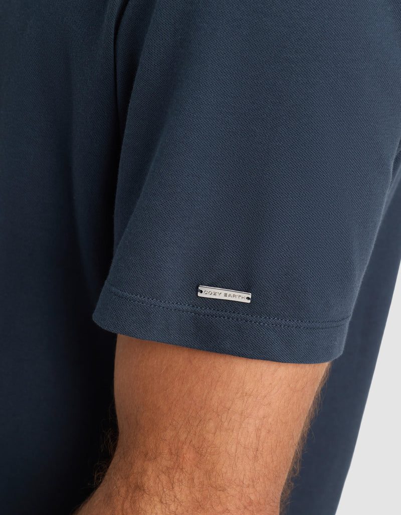 A close-up of a person's arm wearing Cozy Earth's Men's Pique Polo, a short-sleeved dark blue shirt with a small rectangular label near the sleeve hem.
