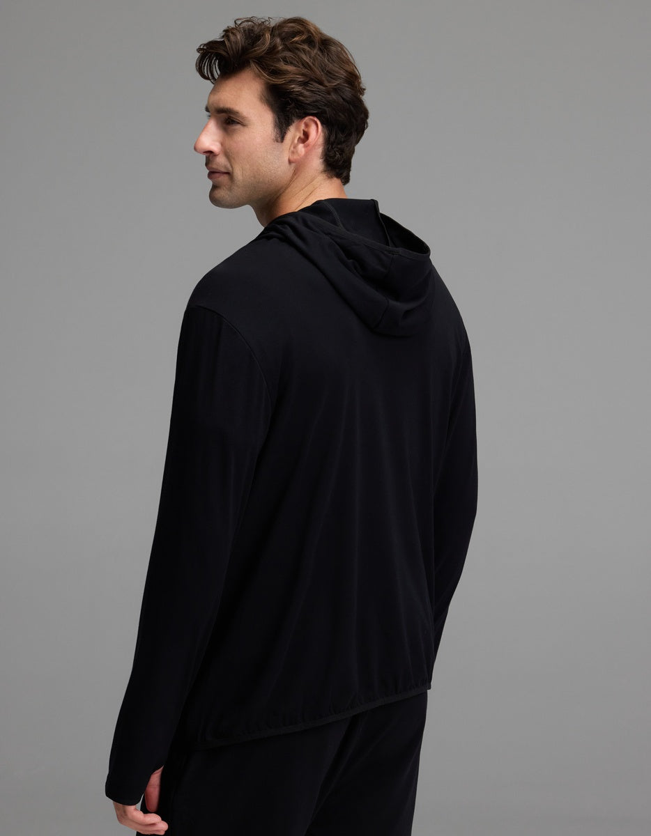 A man with short brown hair is standing and looking to his left, with his back and left side visible against a plain gray background. He is wearing the Cozy Earth Men’s Recovery Hoodie in black.