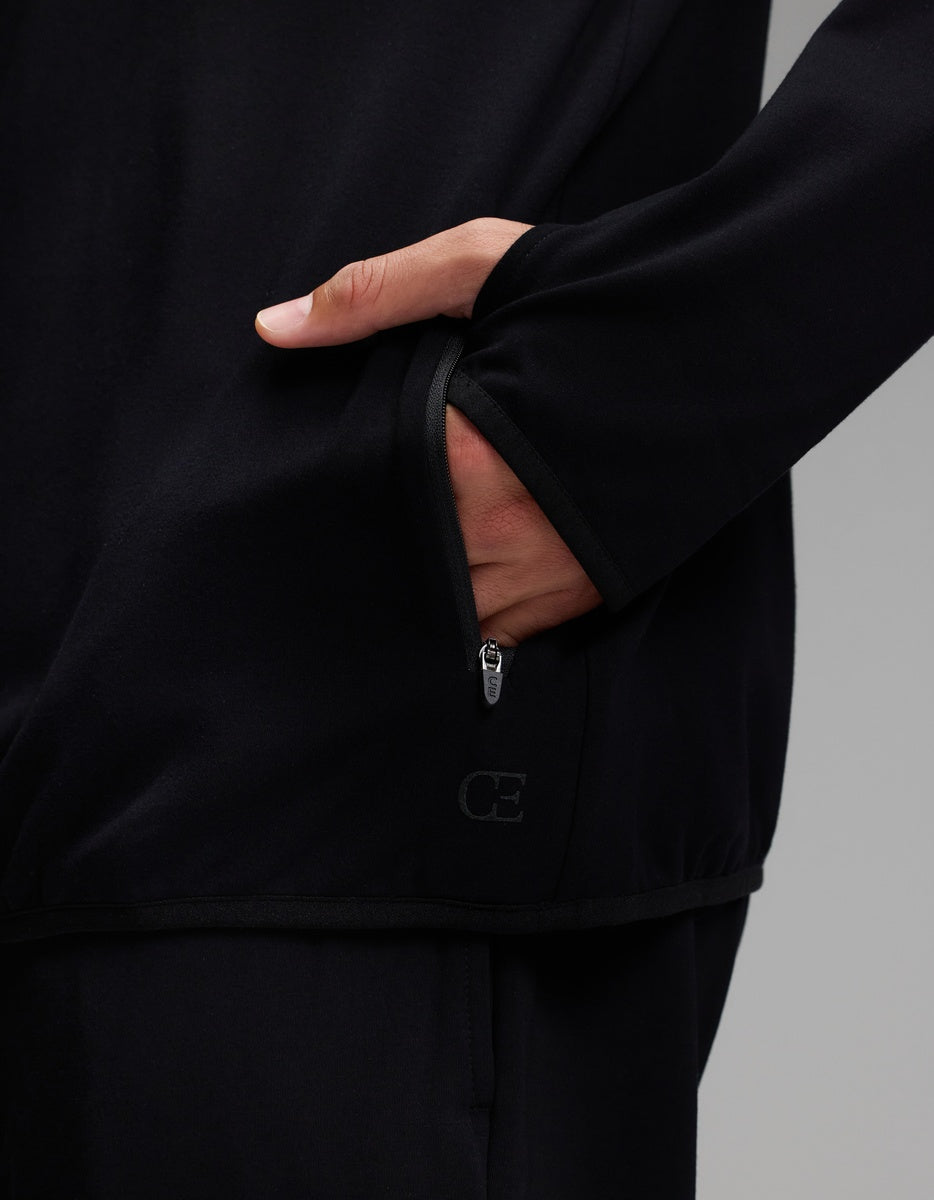 A person wearing the Cozy Earth Men’s Recovery Hoodie in black, with their hand partially inside a zippered pocket. The hoodie features subtle piping along the edges and a small Cozy Earth logo near the bottom of the pocket.