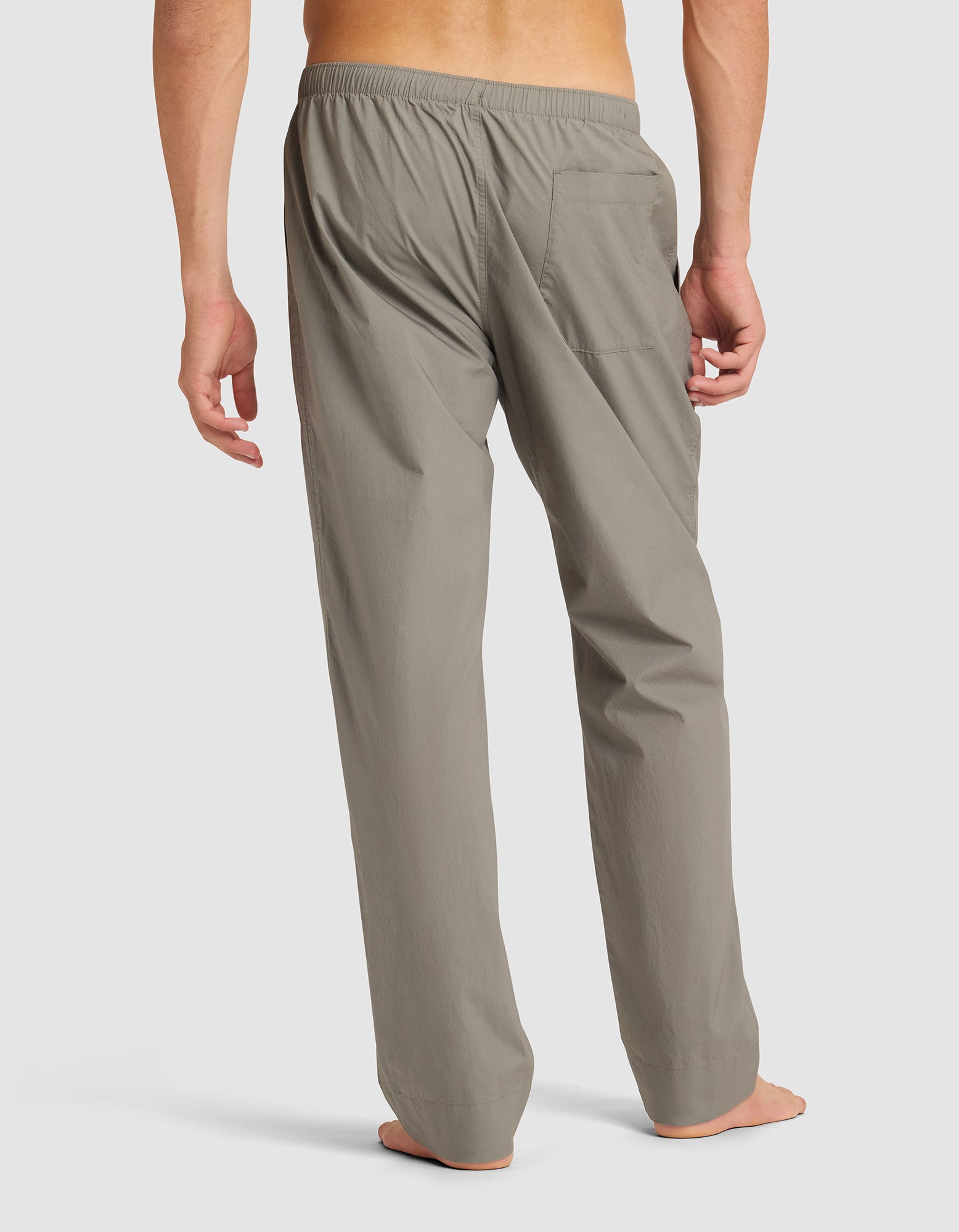 A person stands barefoot, facing away, wearing Cozy Earth Men's Sleep Pant in light gray. The pants are loose-fitting with an elastic waistband and a single right back pocket. Background is plain white. |Color:Cypress