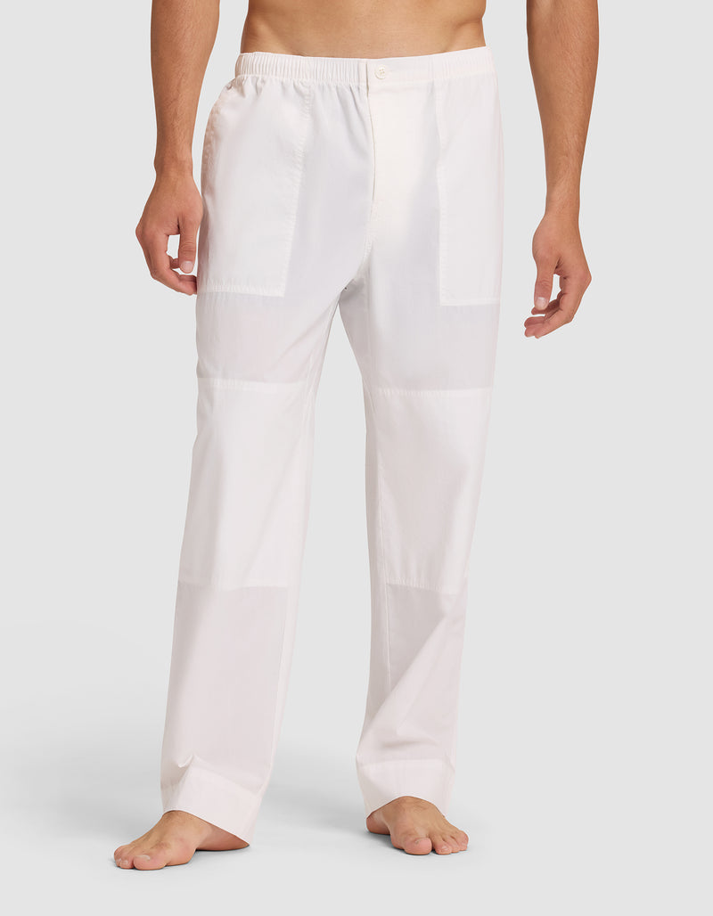A person stands barefoot wearing Cozy Earth Men's Sleep Pant, featuring loose-fitting white fabric with an elastic waistband and button closure; their upper body is not visible.