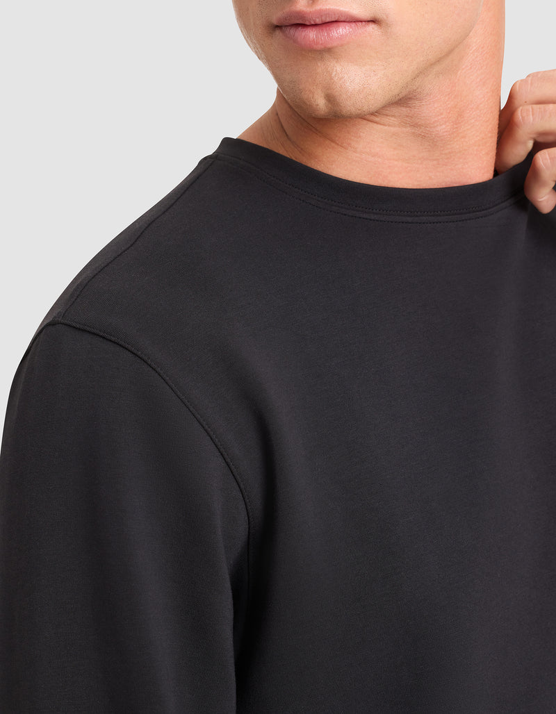 A close-up of a person wearing the Cozy Earth Men's StretchTech Crewneck in black, gently holding the collar. The image displays part of their face, neck, and upper torso.