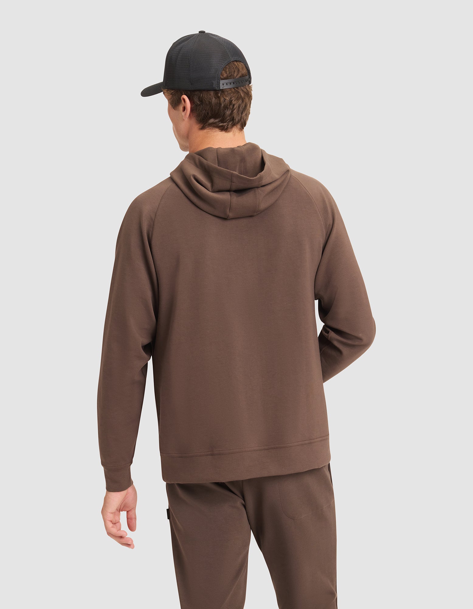 A man wearing the Cozy Earth Men's StretchTech Hoodie stands with his back to the camera against a plain light background.