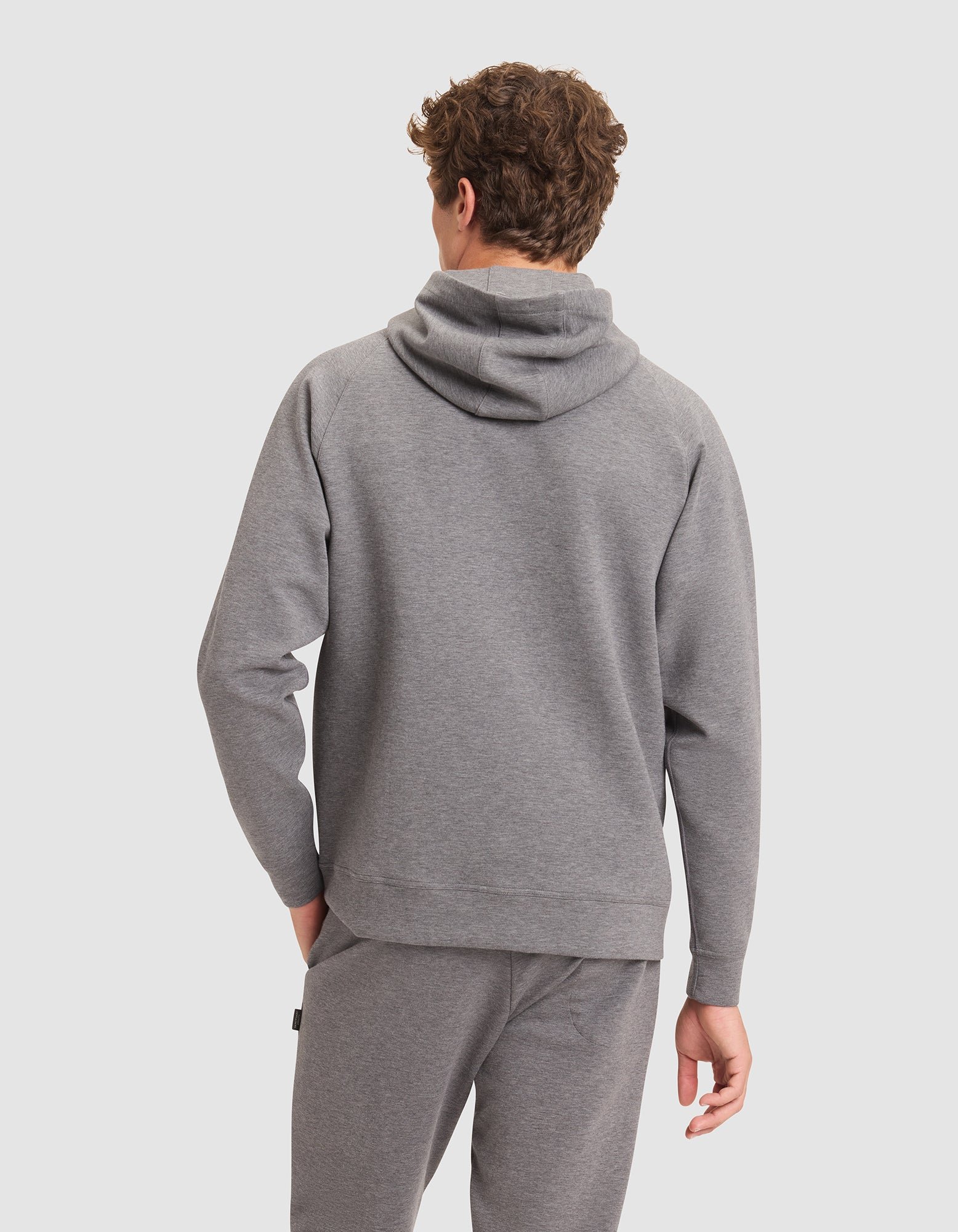 A man with curly hair is seen from behind wearing the Cozy Earth Men's StretchTech Hoodie in gray against a plain light background. |Color:Coal Heather