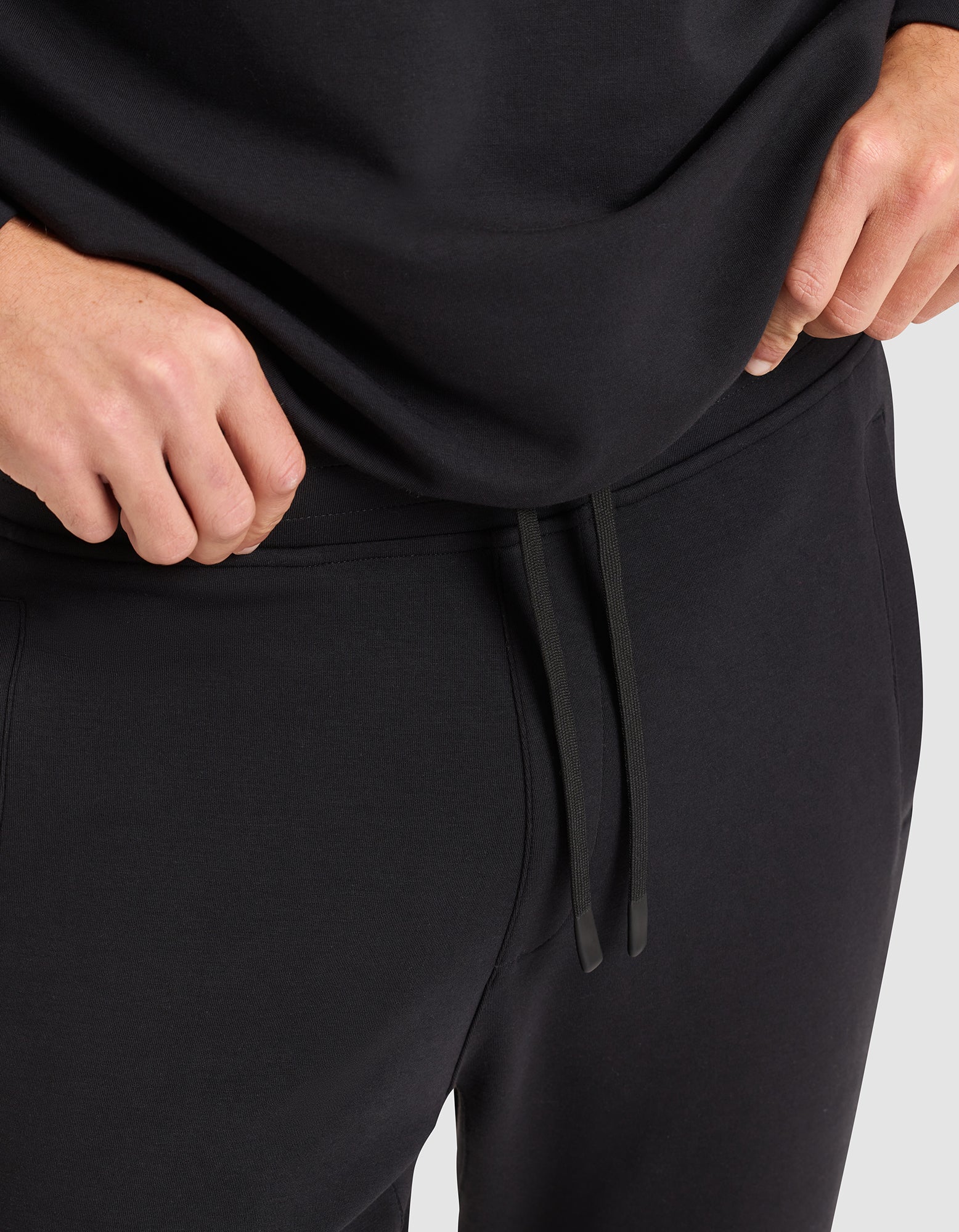 A person wearing Cozy Earth's Men's StretchTech Jogger, featuring a drawstring waist, stands with their hands near their waist. 