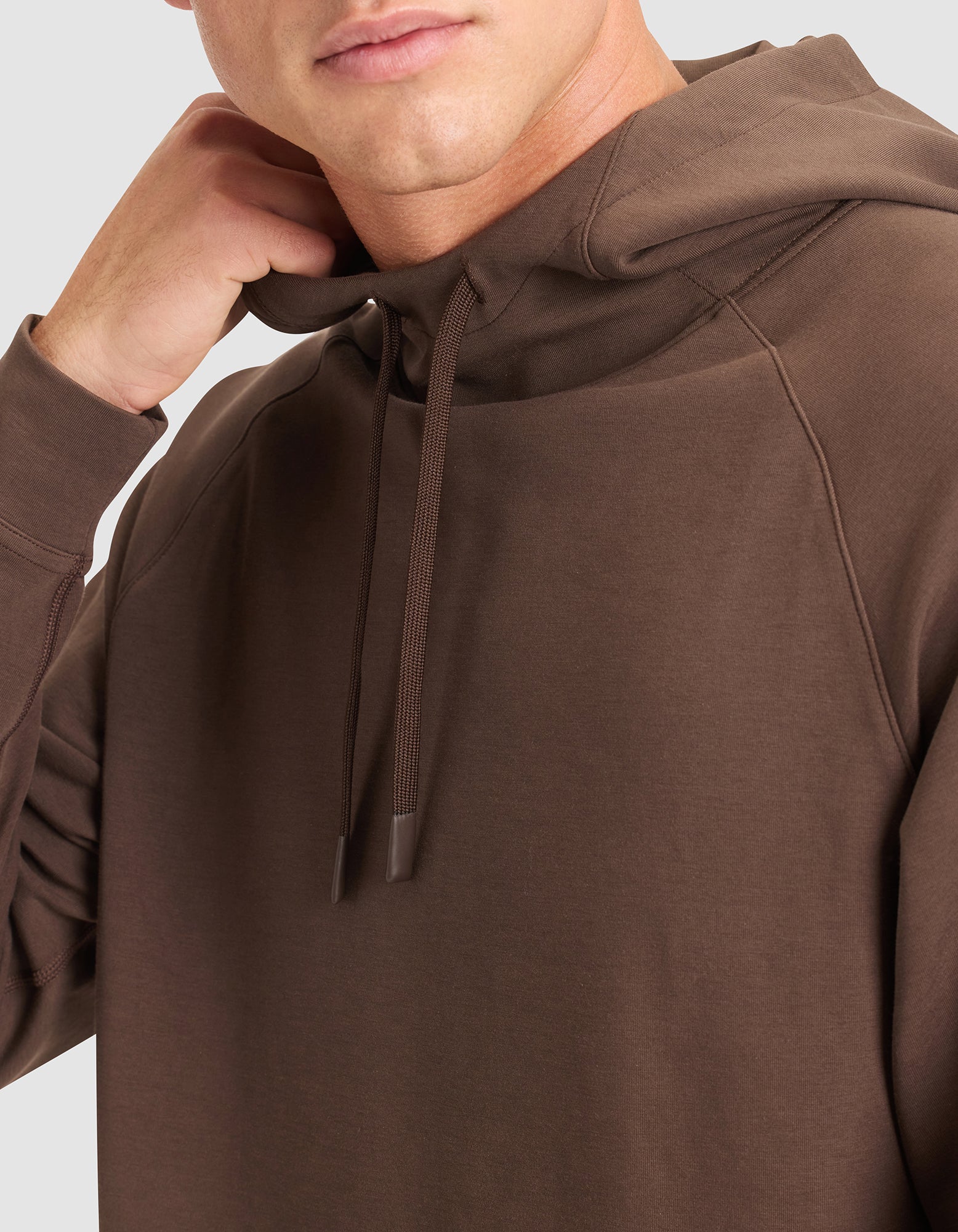 A person, shown from the shoulders up, touches their neck while wearing the Cozy Earth Men's StretchTech Hoodie with drawstrings. The background is light gray.  