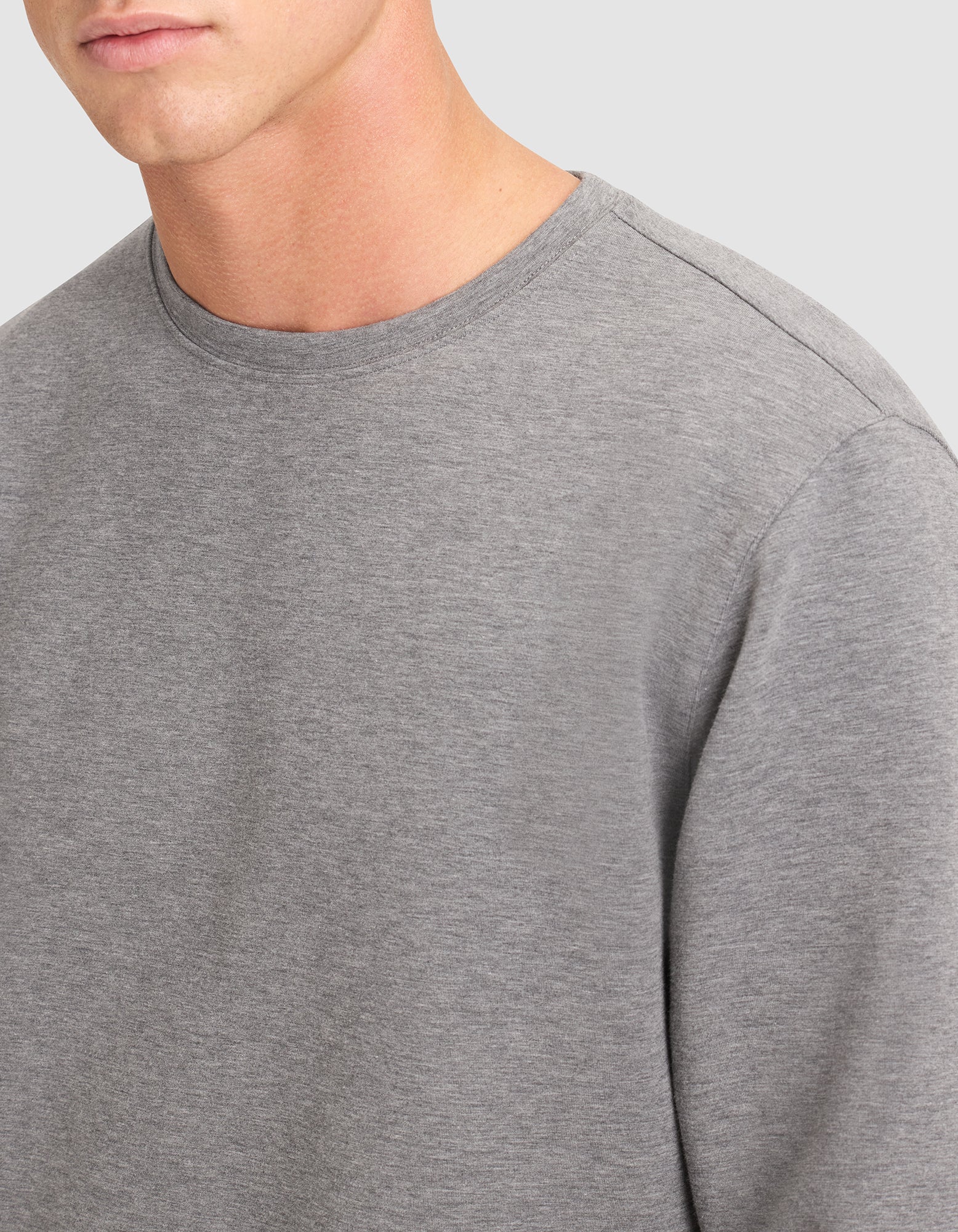 A close-up of a person wearing the Cozy Earth Men's StretchTech Crewneck & Jogger Set in grey, shown from shoulders to upper chest against a light grey background. 