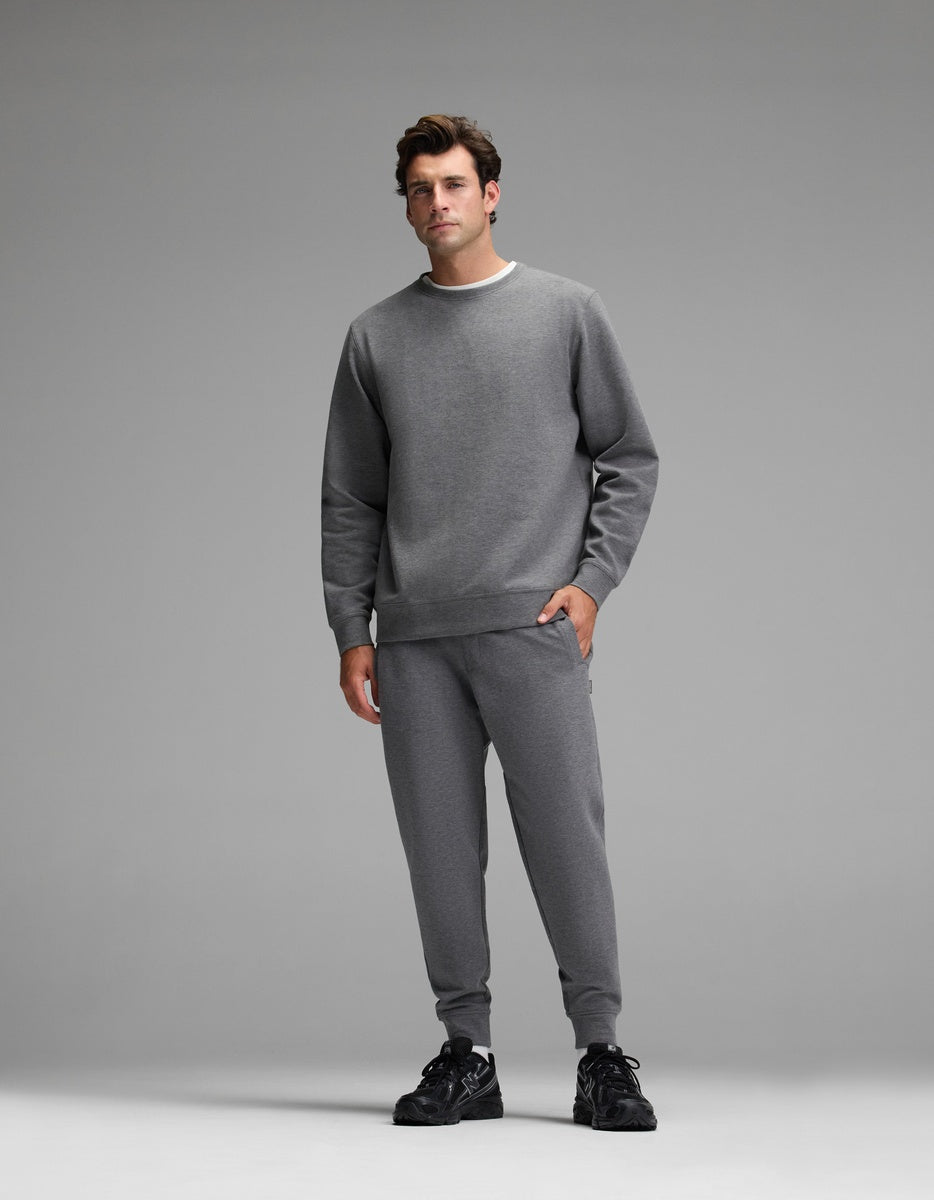 A man stands facing forward, wearing the Cozy Earth Men’s StretchTech Crewneck & Jogger Set in gray with black sneakers, set against a plain gray background.|Color:Coal Heather