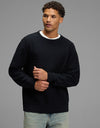 A man wears a jet black Men’s Tate Crewneck sweater with a subtle ribbed texture over a white t-shirt and light-wash jeans.|Color:Jet Black