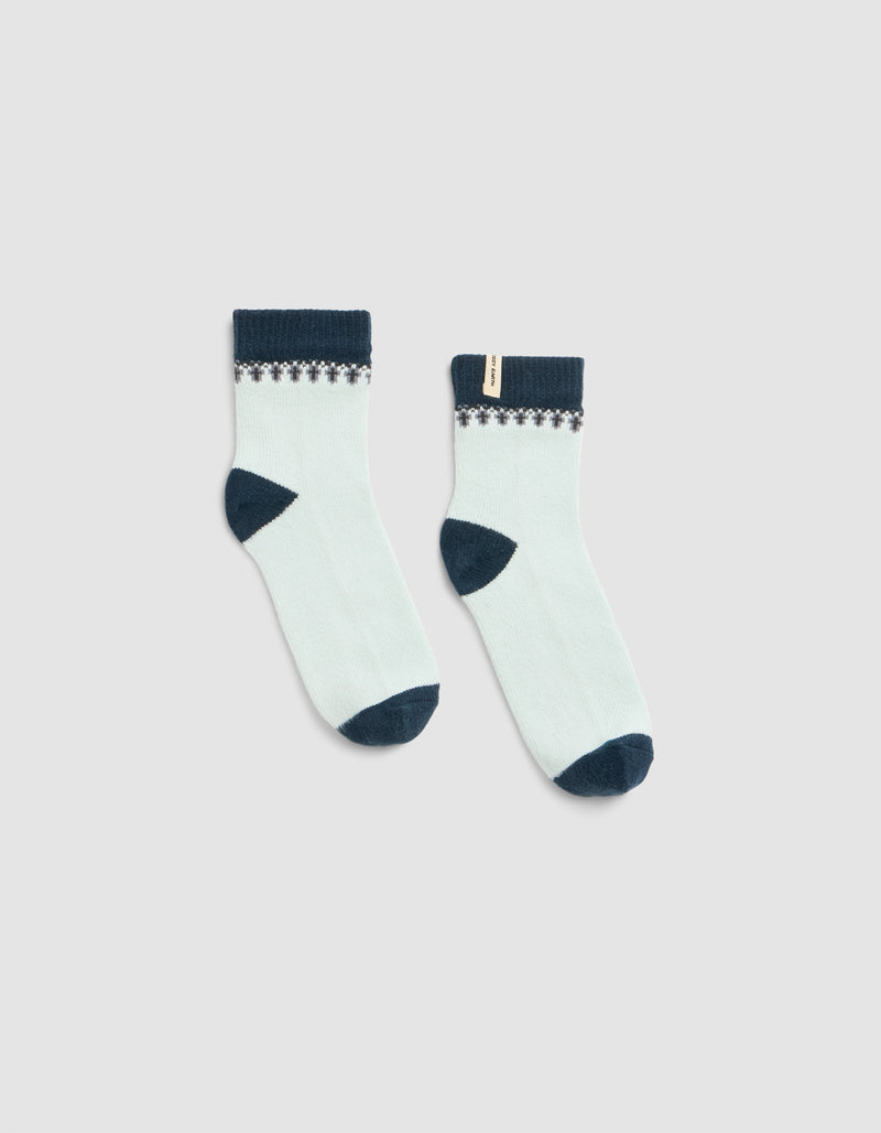 The Mistletoe Plush Modern Crew Sock by Cozy Earth is a white ankle sock with dark blue toes, heels, and cuffs, featuring a small decorative pattern near the top and a beige tag on one sock.