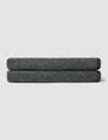 Two neatly folded Cozy Earth Nantucket Bath Sheets in dark gray are stacked on top of each other against a plain light gray background.|Color:Graphite