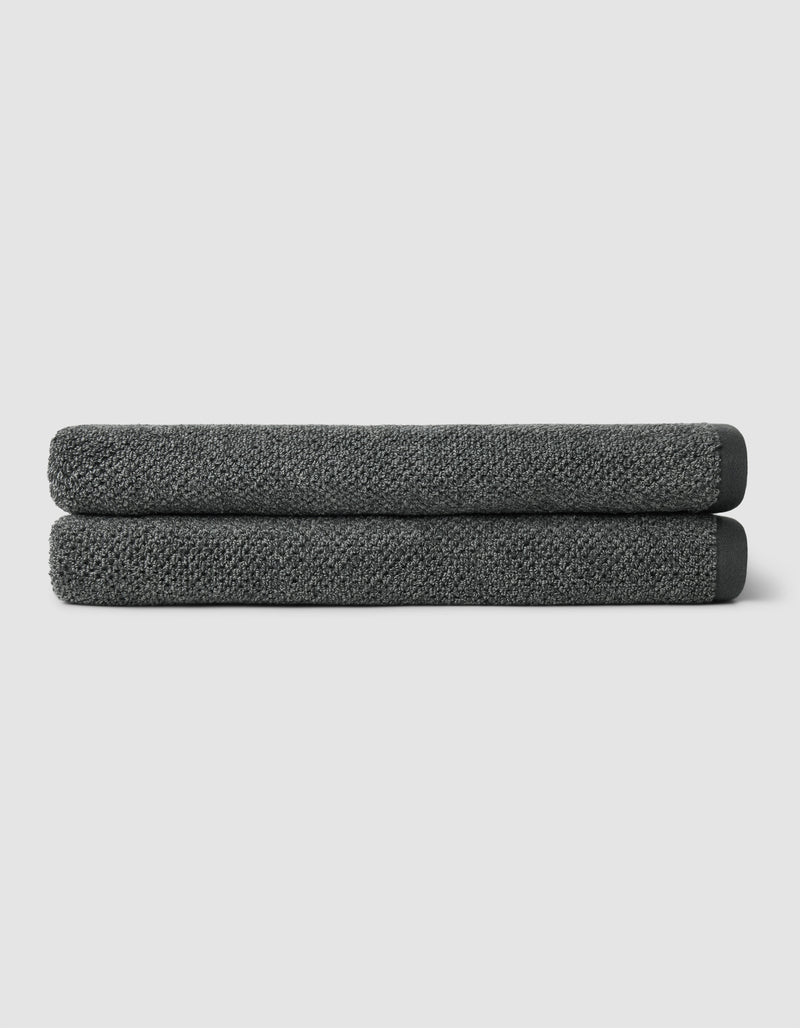 Two neatly folded Cozy Earth Nantucket Bath Sheets in dark gray are stacked on top of each other against a plain light gray background.