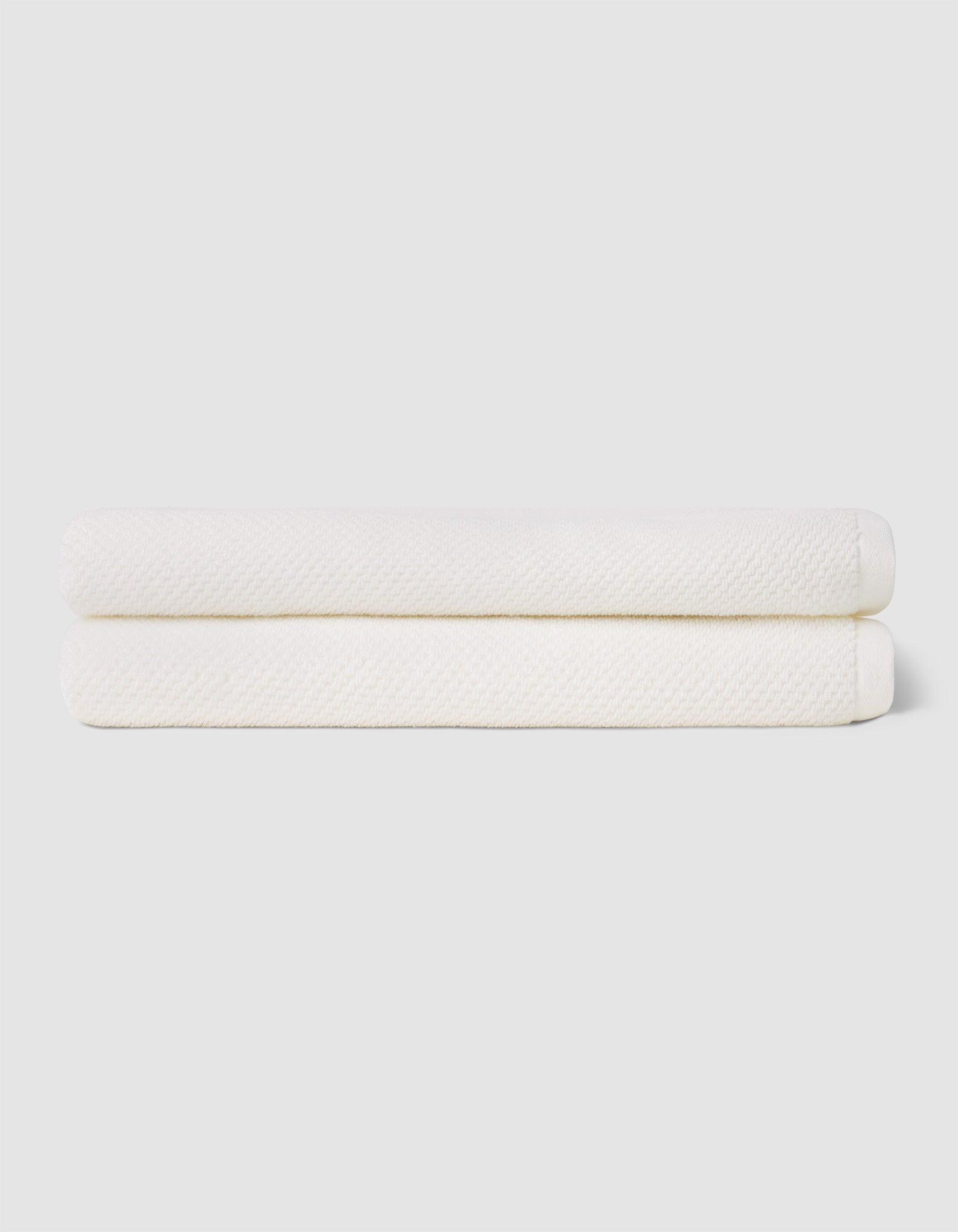 Two neatly folded Cozy Earth Nantucket Bath Sheets are stacked atop each other against a plain, light-colored background.