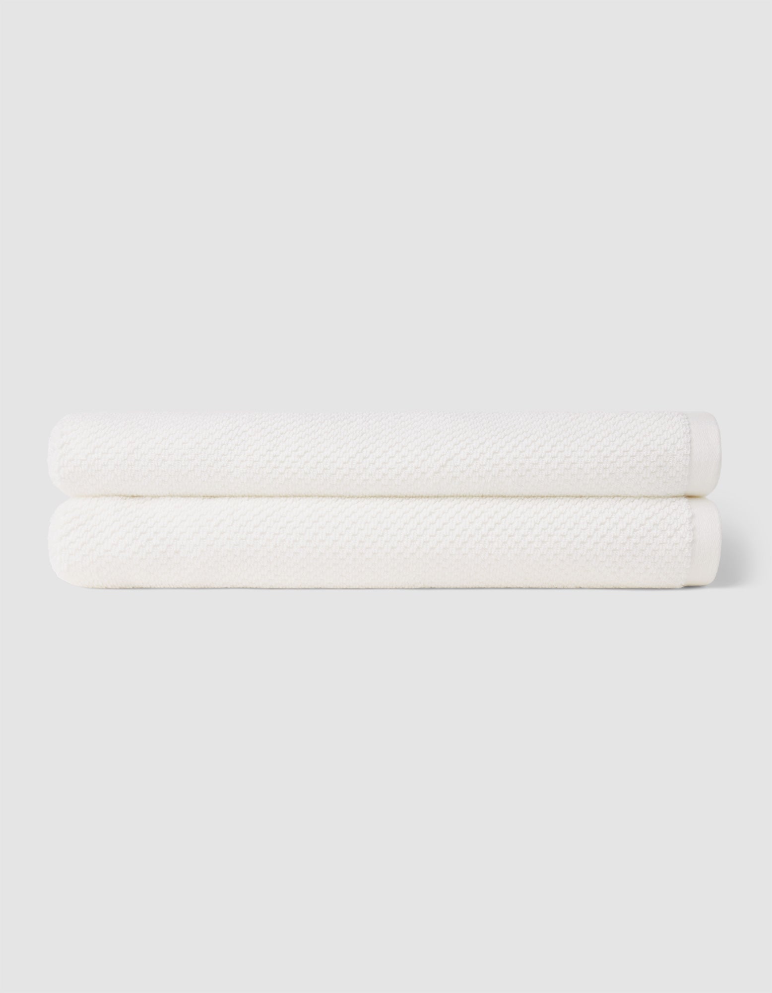 Two neatly folded Nantucket Bath Towels by Cozy Earth are stacked together against a plain light gray background.|Color:White
