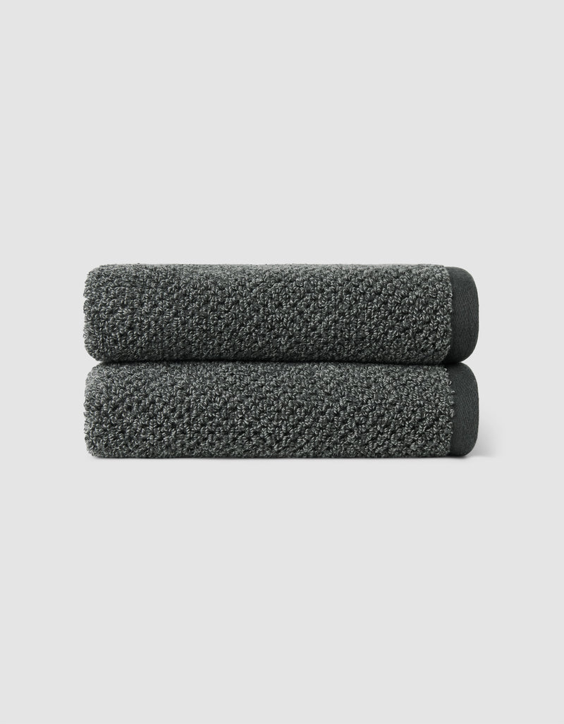 Two dark gray Nantucket Hand Towels by Cozy Earth, neatly rolled and stacked, set against a plain light gray background.