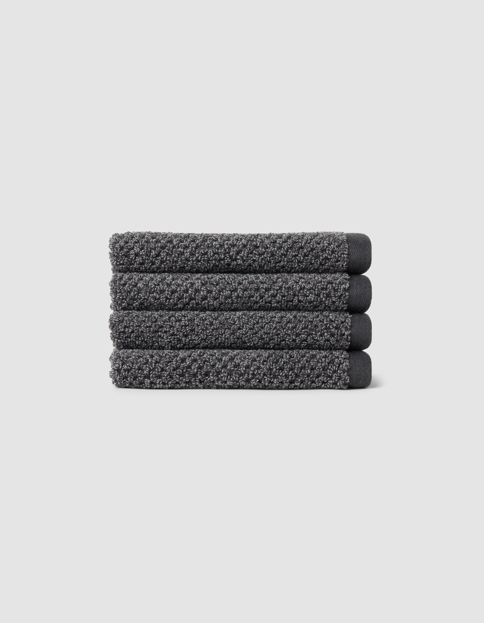 Four neatly folded Nantucket Washcloths by Cozy Earth, textured in dark gray, are stacked horizontally on a plain light gray background.