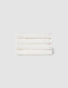 Four neatly folded Nantucket Washcloths by Cozy Earth, stacked horizontally against a plain light gray background.|Color:White