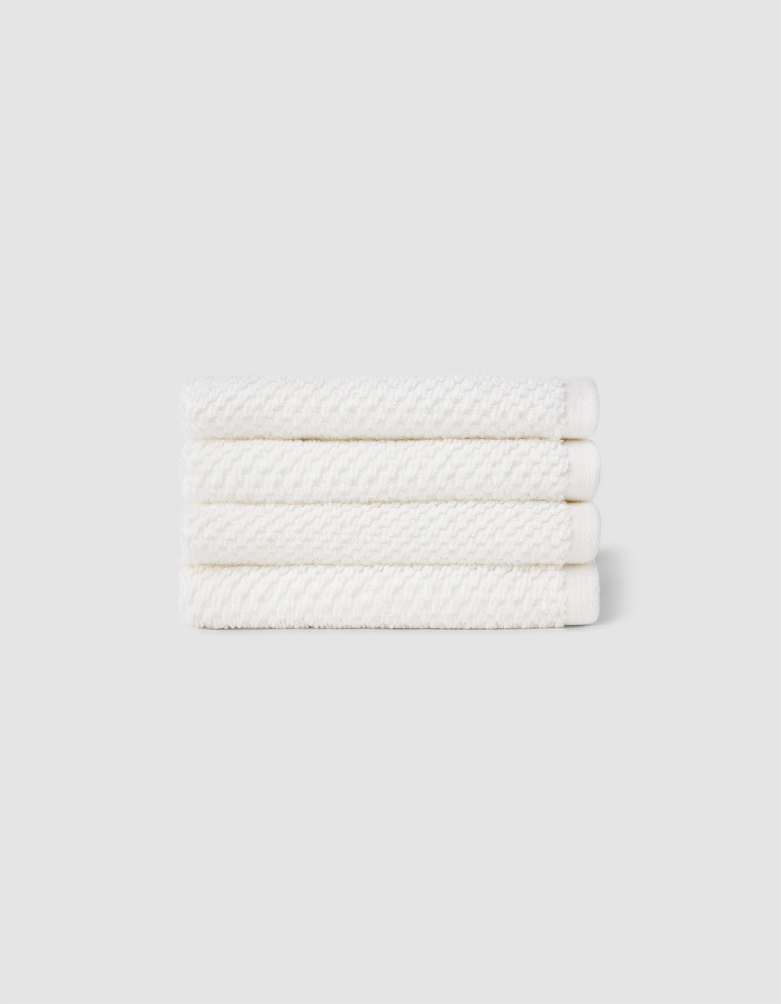 Four neatly folded Nantucket Washcloths by Cozy Earth, stacked horizontally against a plain light gray background.