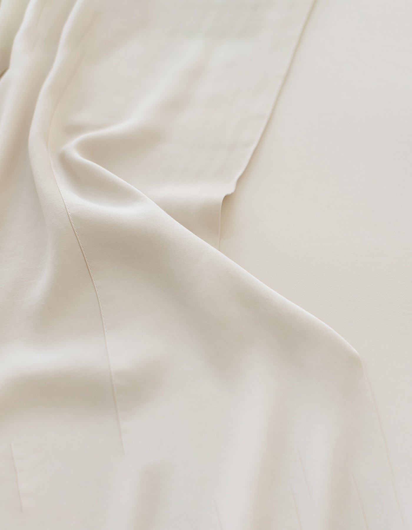 Close-up of Cozy Earth's Bamboo Sheet Set in a soft, light beige tone featuring smooth folds and creases. The fabric has a silky sheen, exuding elegance and simplicity. 