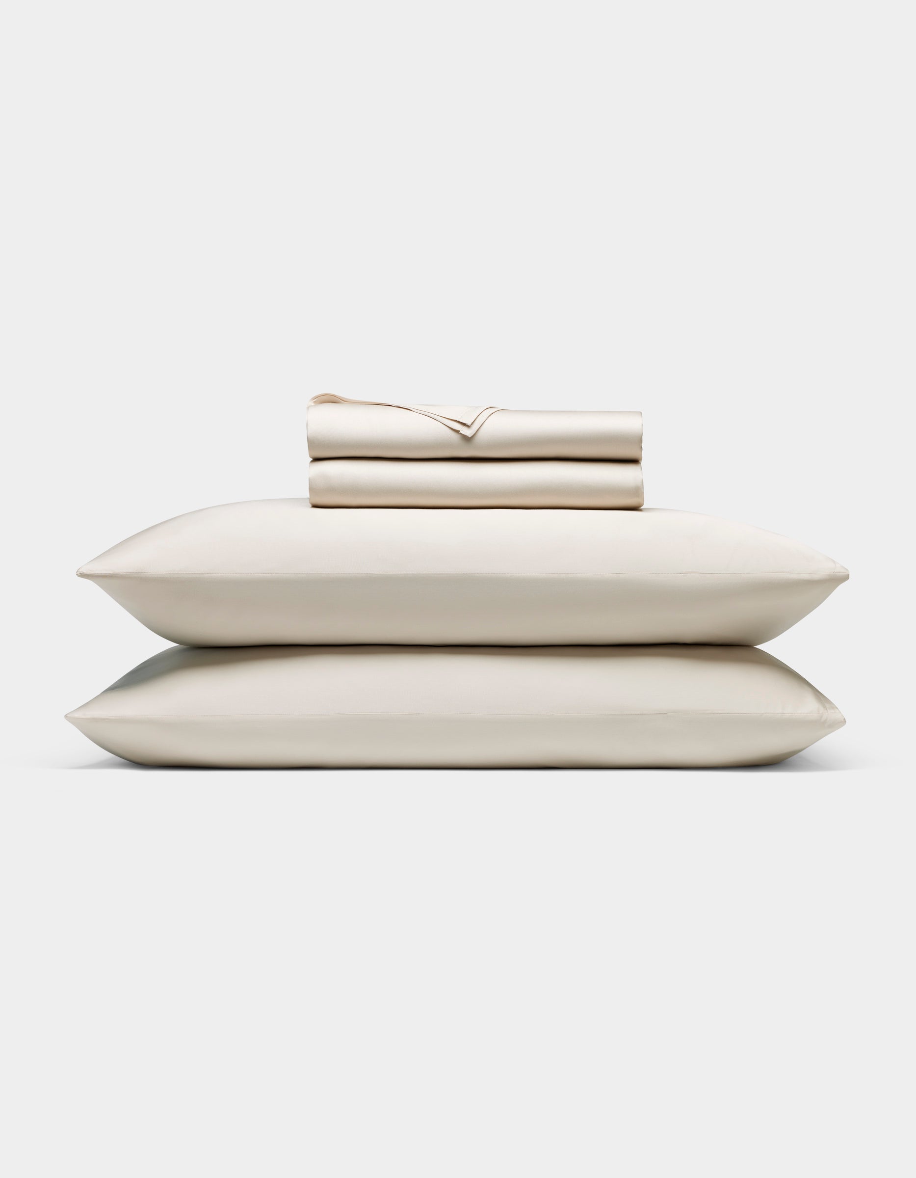 The Bamboo Bedding Ultimate Bundle by Cozy Earth features two cream-colored pillows stacked with a folded matching sheet set on top, all displayed against a plain white background.|Color:Oat