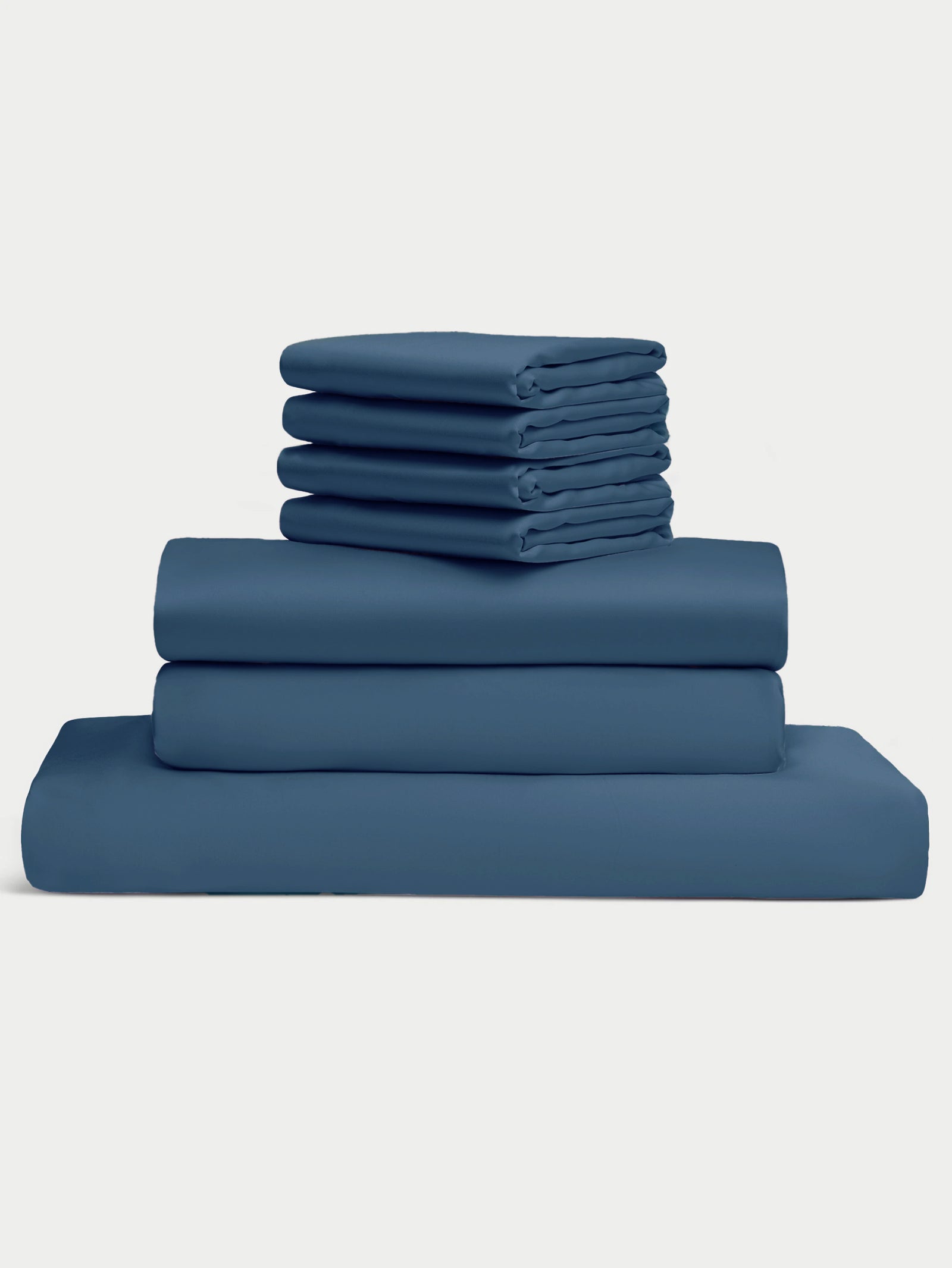 A neatly folded stack of the Bamboo Bedding Core Bundle by Cozy Earth, featuring pillowcases, fitted sheets, and flat sheets in dark teal, is arranged on a plain white background. 