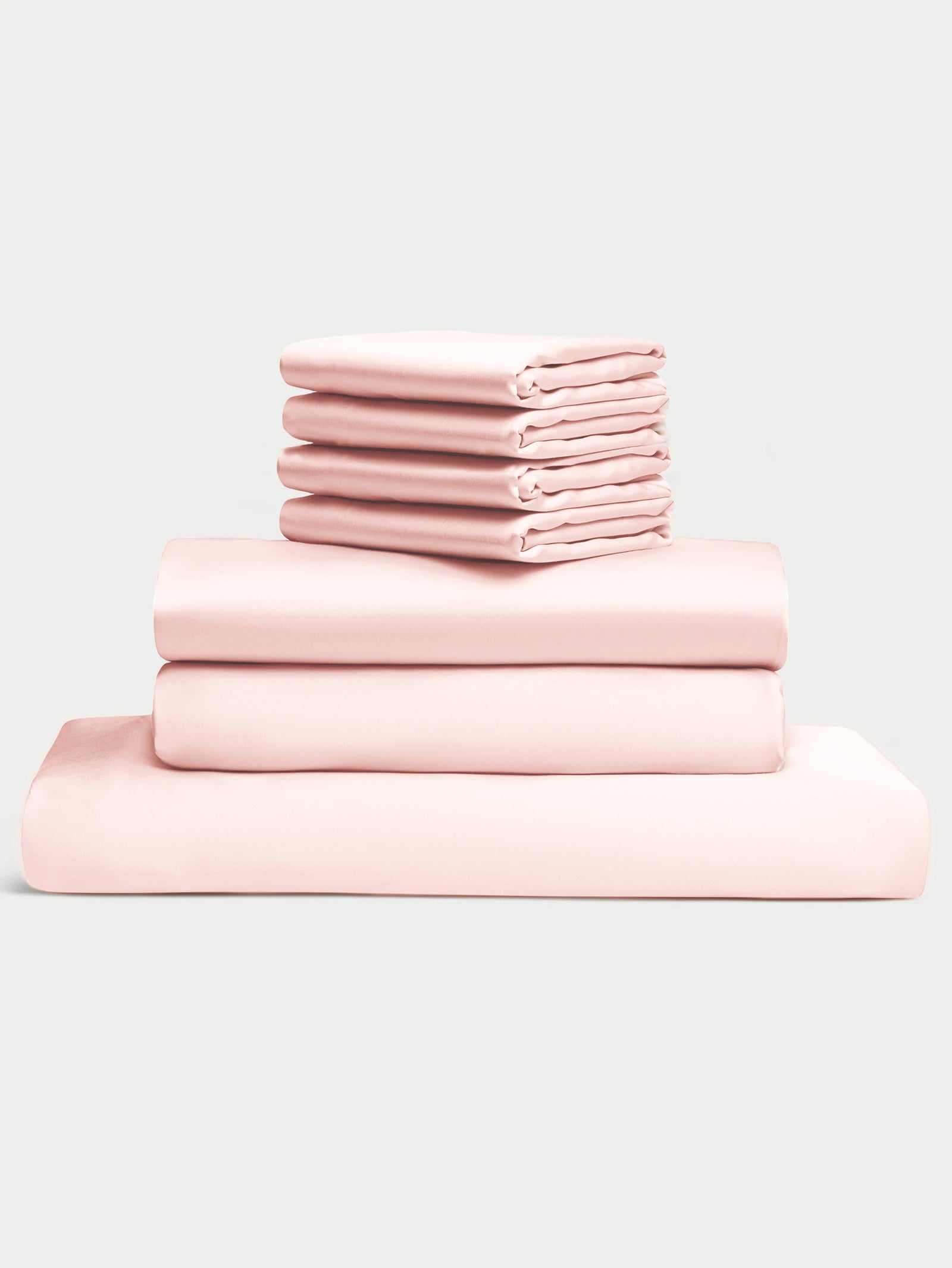 The Bamboo Bedding Core Bundle by Cozy Earth features a neatly folded stack of light pink sheets and pillowcases, including two larger sheets and four smaller pillowcases, set against a plain background. 