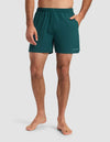 A barefoot man stands against a plain background, wearing Cozy Earth Men's Day & Night Short 5" in teal with an elastic waistband and one hand in his pocket.|Color:Adrift