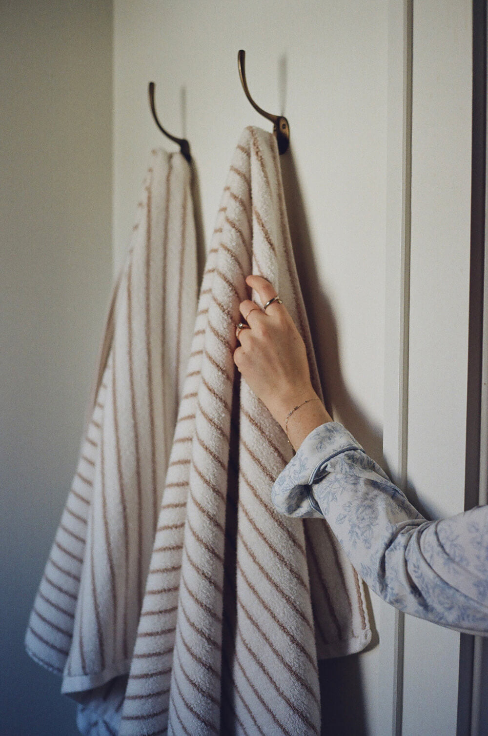 Striped towel hanging on a hook with a hand reaching out to grab it.