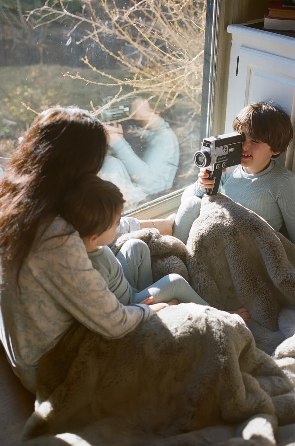 Two children and a woman playing with vintage video cameras by a window