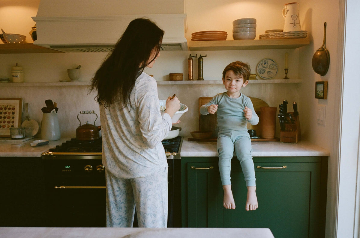 Woman and child in a kitchen, with the woman holding a plate and the child standing on a counter.