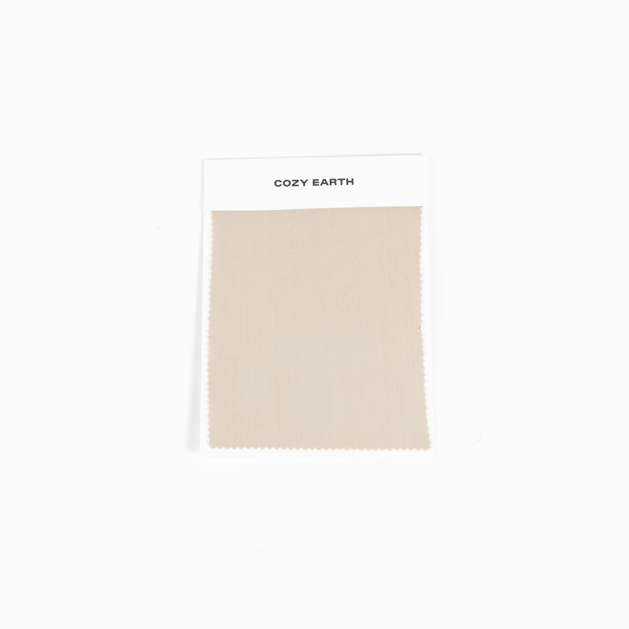 A square fabric sample from Cozy Earth, identified as the Bamboo Sheet Swatch. The swatch is a simple beige color with a zigzag edge design and is attached to a white card. |Color:Driftwood