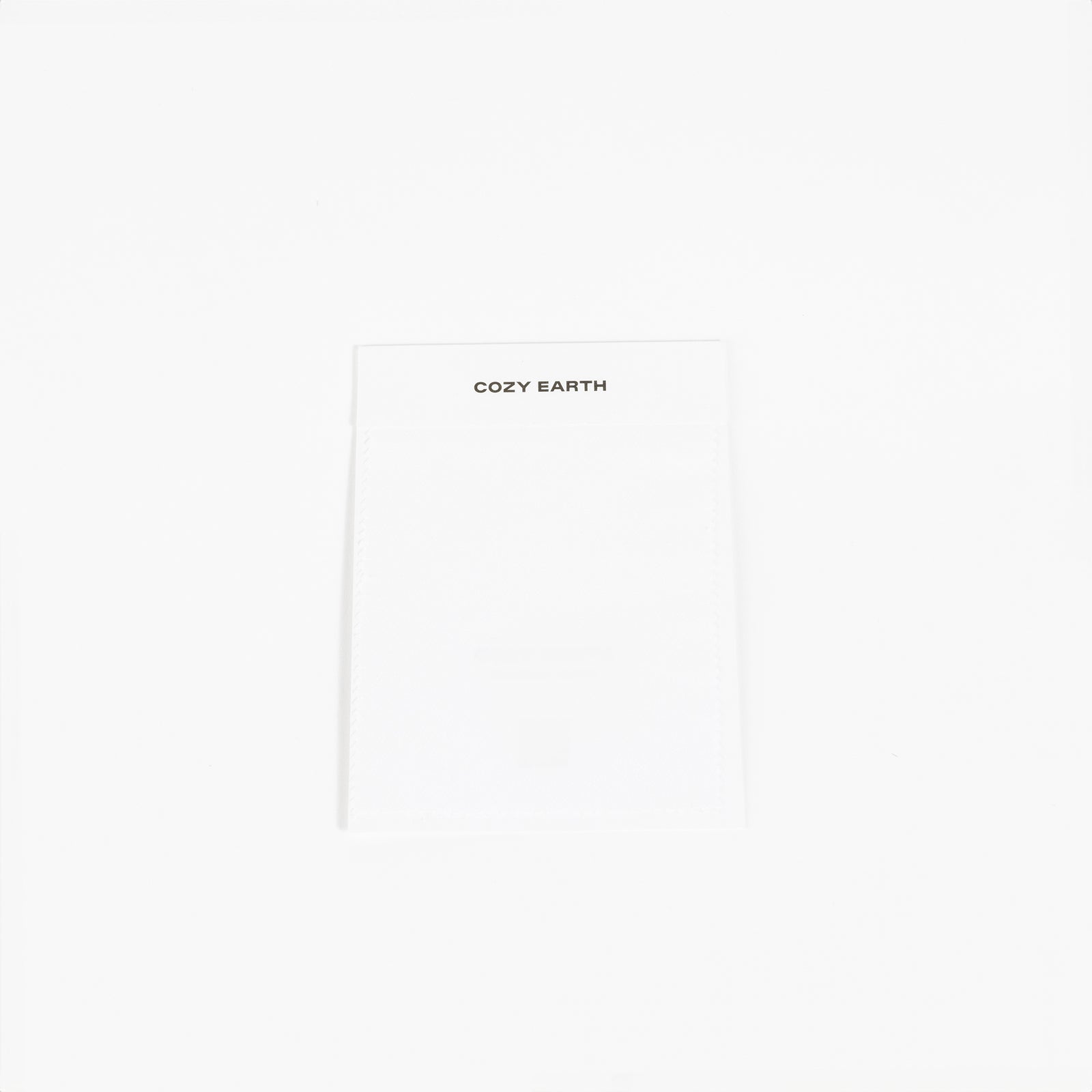 A white fabric label prominently displays the brand name "Cozy Earth" at the top, set against a plain white background to highlight its minimalist design. 