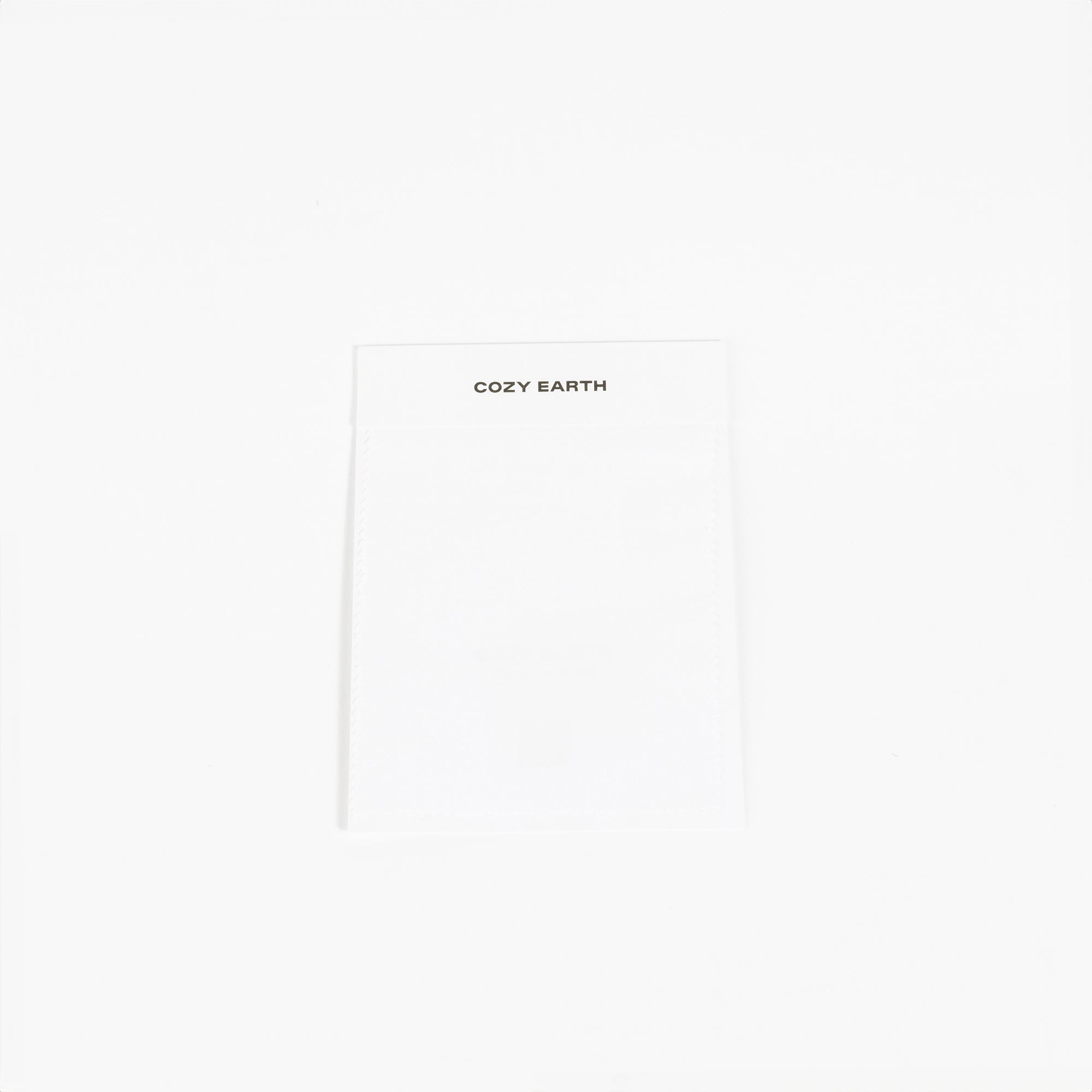 A white fabric label prominently displays the brand name "Cozy Earth" at the top, set against a plain white background to highlight its minimalist design. 