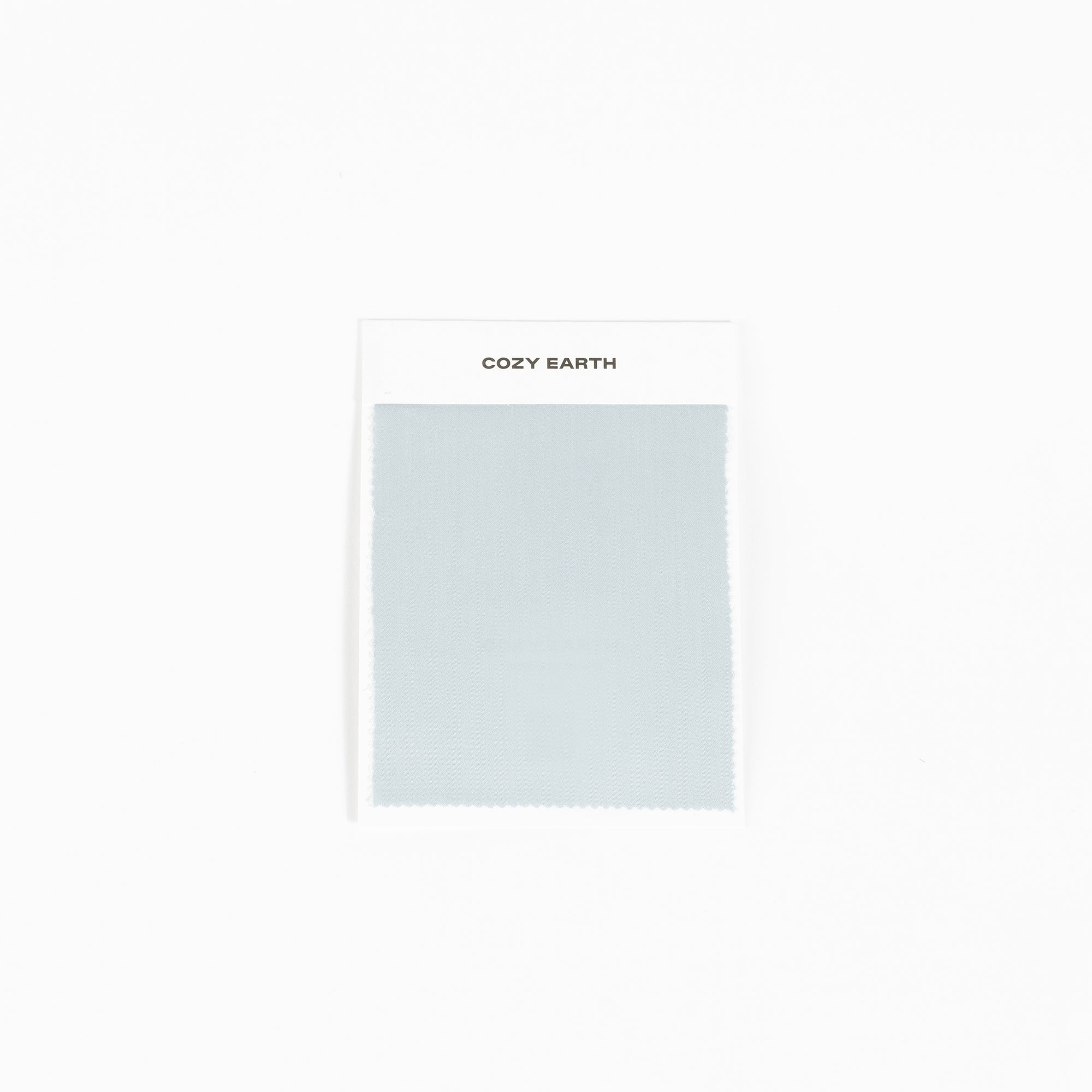 A sample of the bamboo sheet fabric in light gray is displayed against a white background, mounted on a card labeled with "Cozy Earth" at the top. 