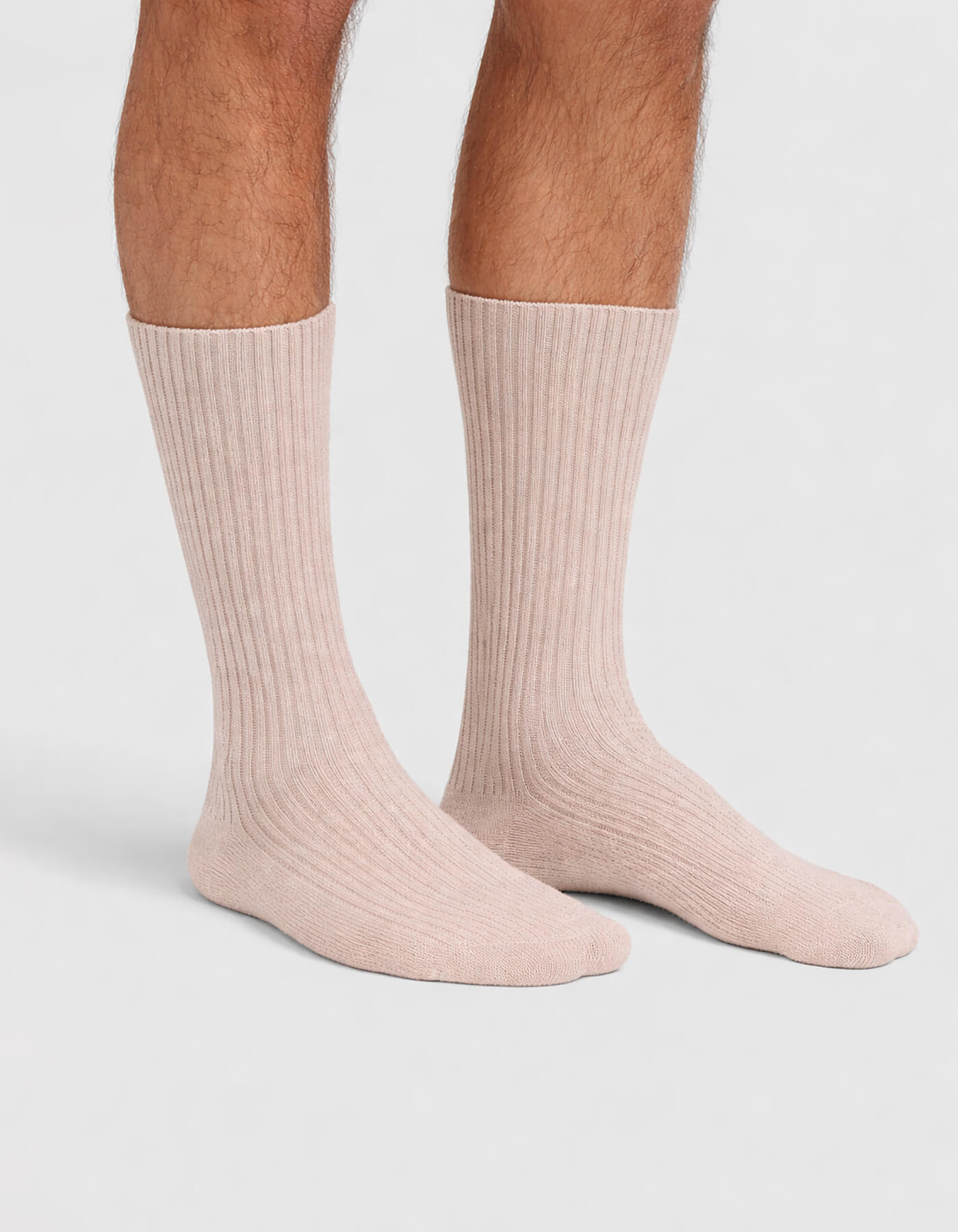 A person wears Cozy Earth's Men's Plush Lounge Calf Socks in light pink, standing on a white background with only their lower legs and feet visible.
